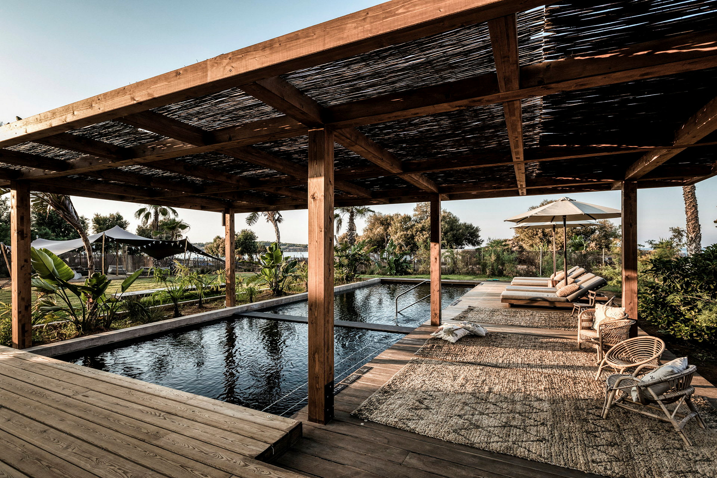 Pulstrande pool under en träpergola med vilstolar och grönskande omgivningar. (AI-genererad text)