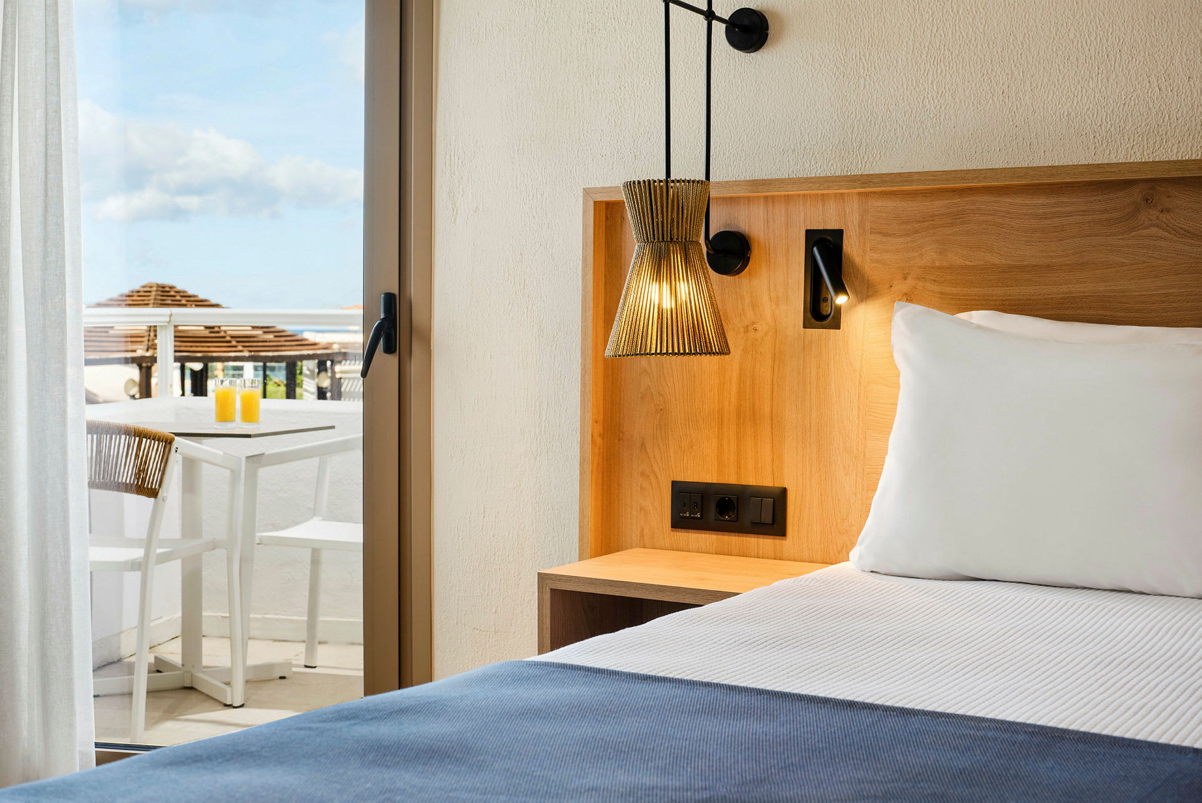 Hotellrum med en säng, träinredning, och en terrass med bord och stolar i bakgrunden. (AI-genererad text)