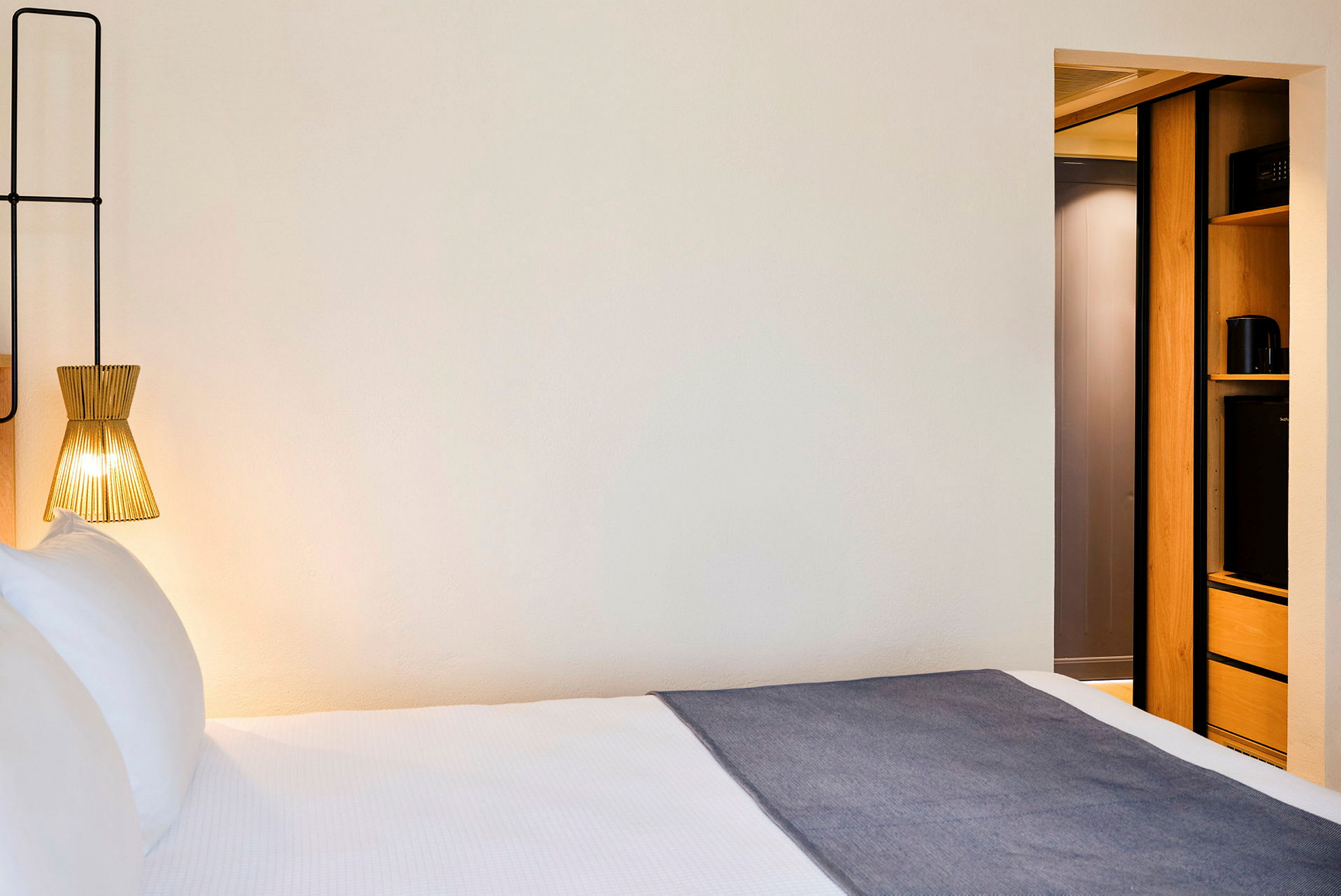 Ett hotellrum med en säng, en modern lampa och en del av inredning med förvaringsutrymme. (AI-genererad text)