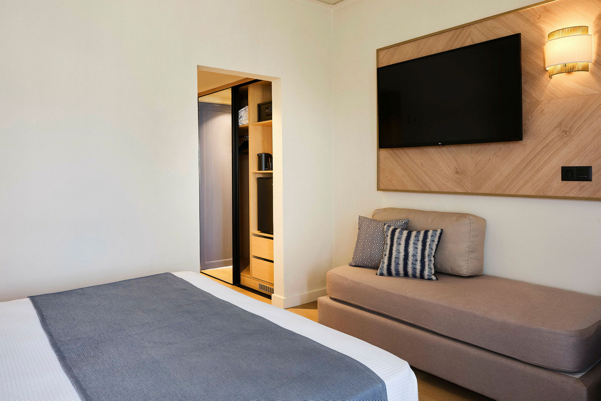 Ett hotellrum med en säng, en soffa, en väggmonterad TV och en öppen garderob. (AI-genererad text)