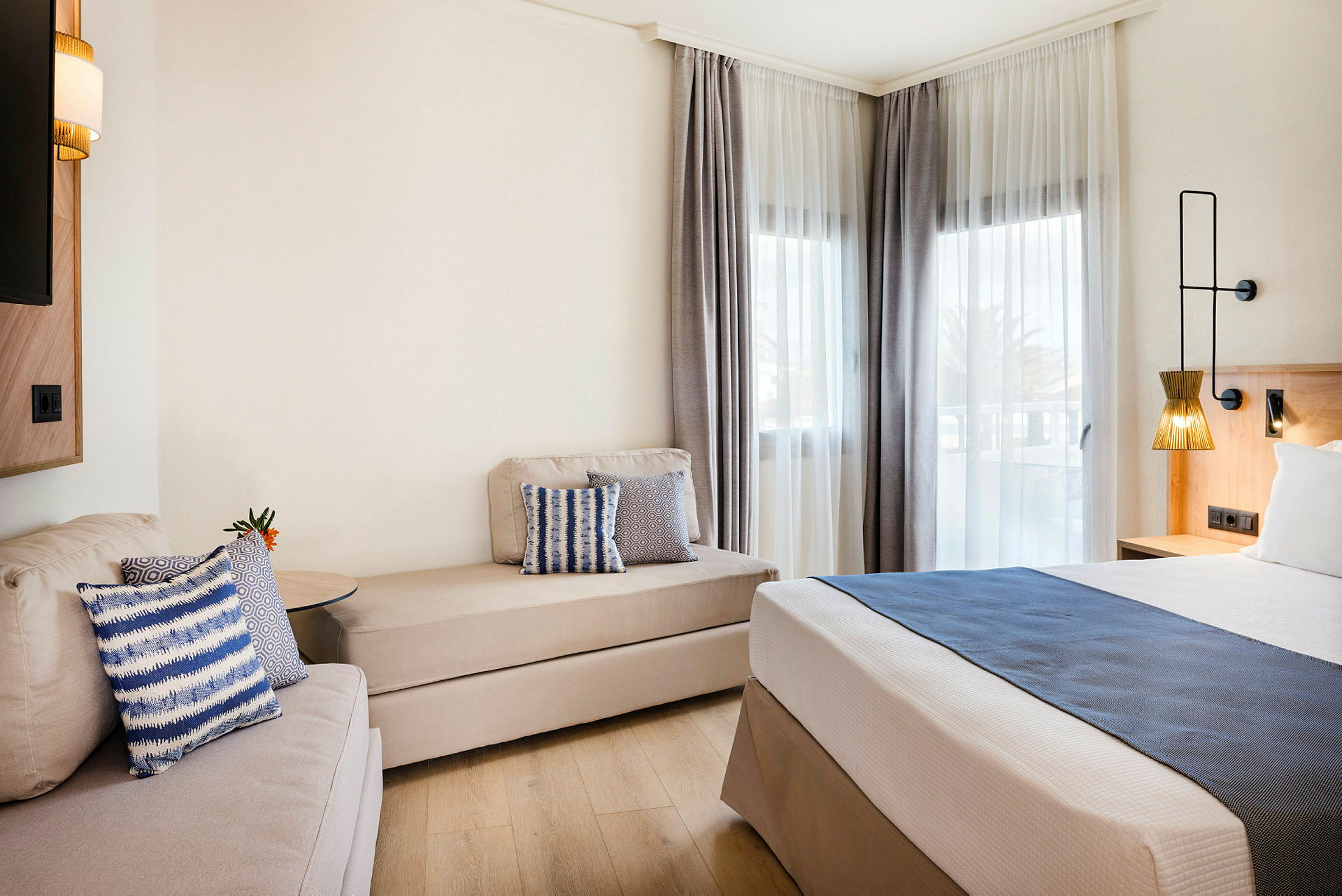 Modernt hotellrum med säng, soffa och fönster med ljusa gardiner. (AI-genererad text)