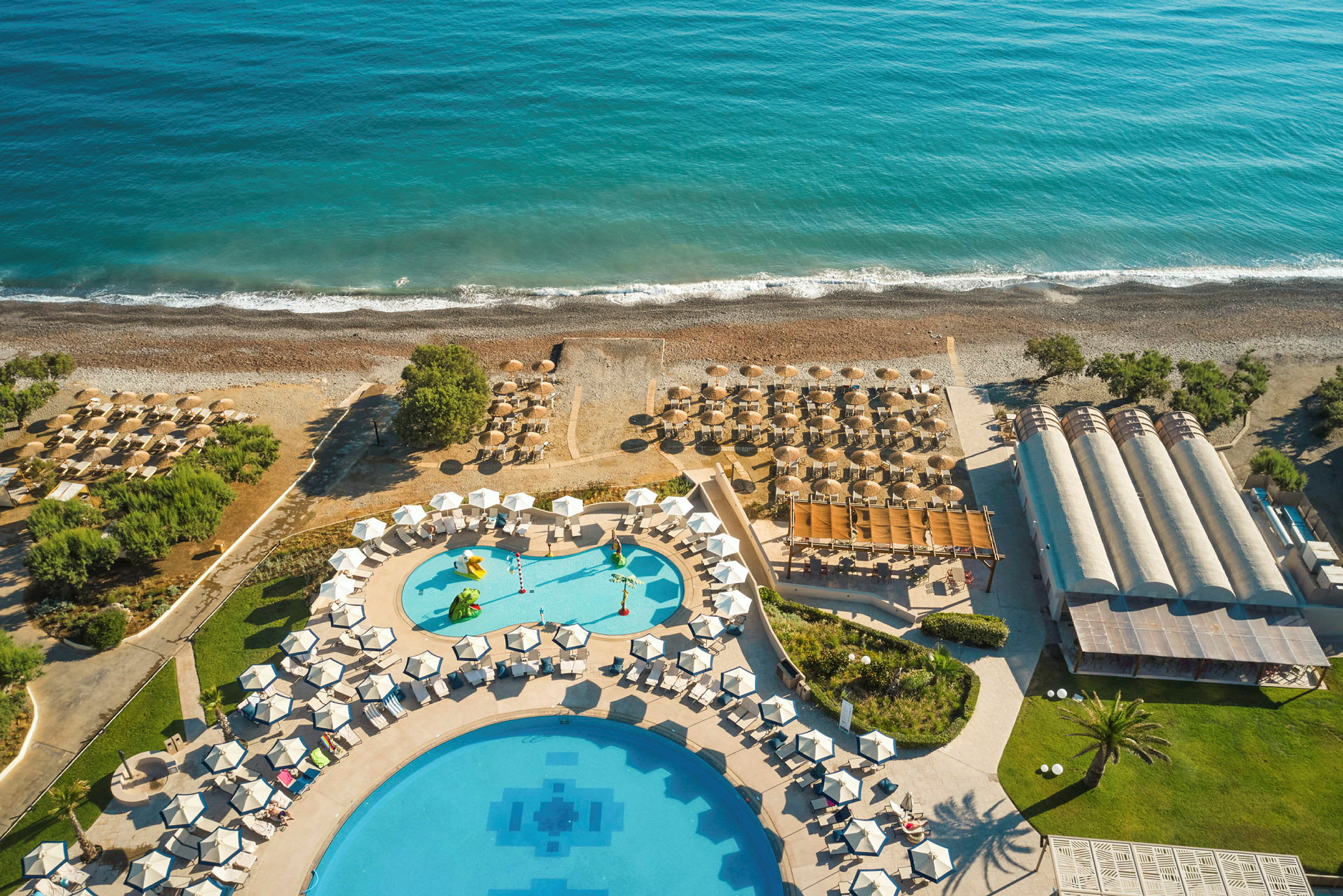 Flygvy över hotellområde med pooler, parasoller och stranden vid havet. (AI-genererad text)