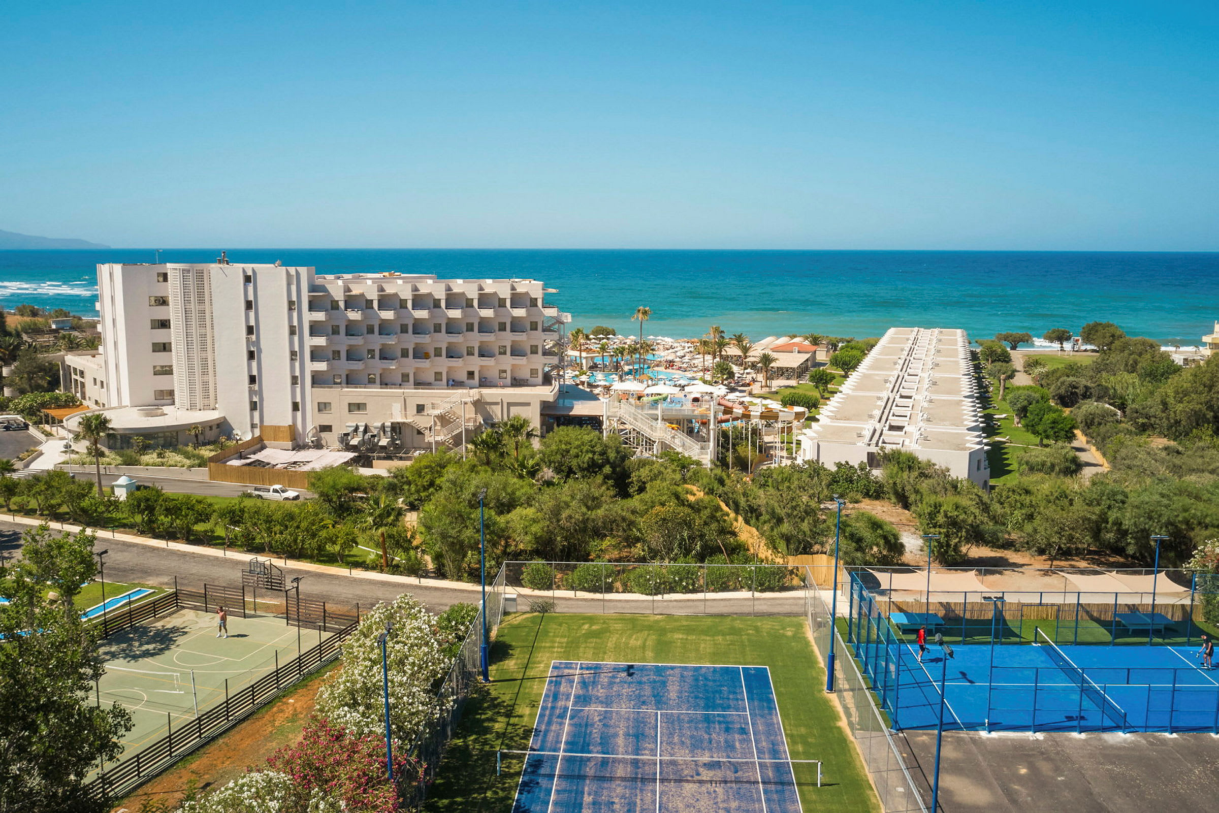 Hotellbyggnad med tennisbanor i förgrunden och havet i bakgrunden. (AI-genererad text)