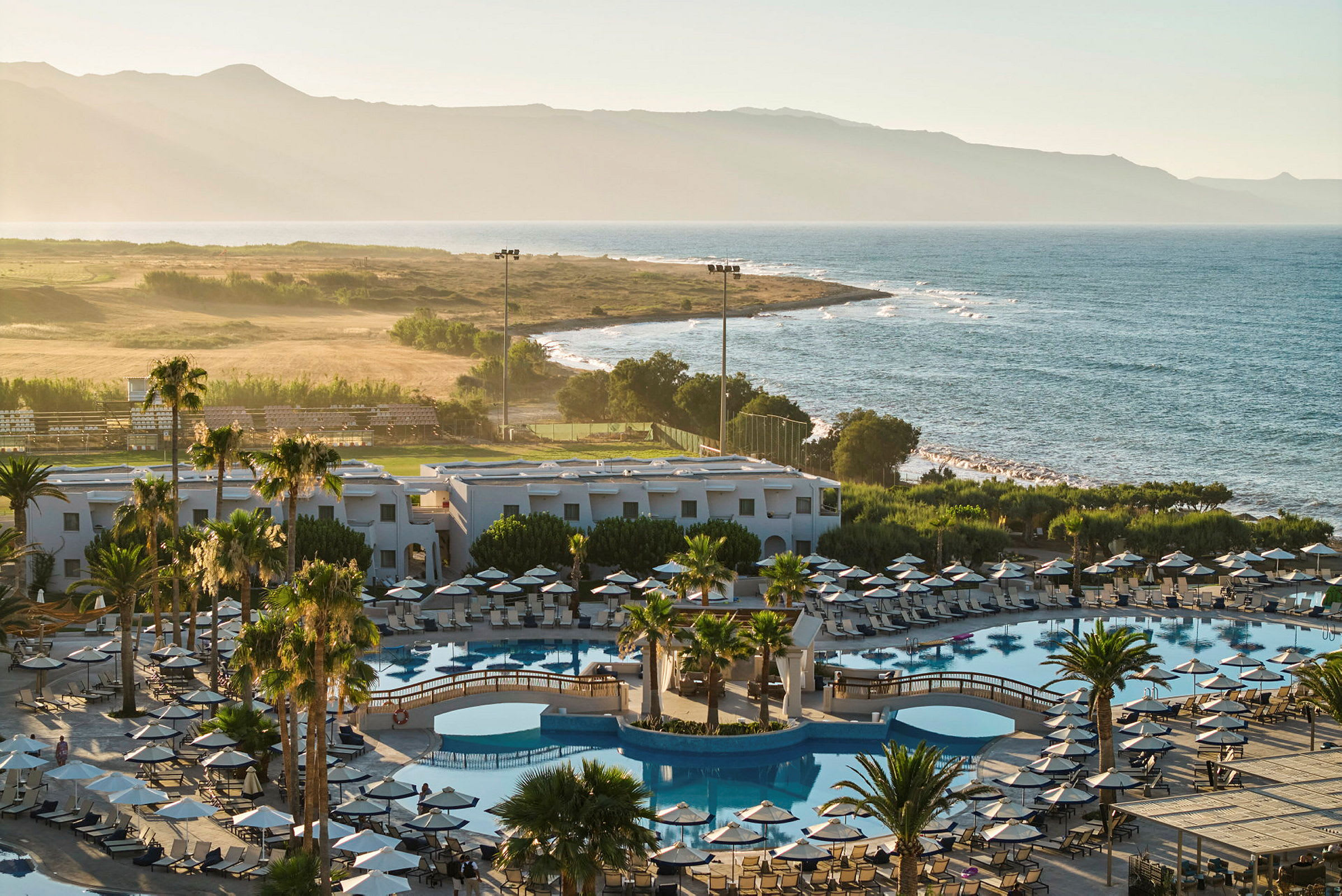 Ett hotellkomplex med swimmingpooler, solstolar och parasoller nära havet. (AI-genererad text)
