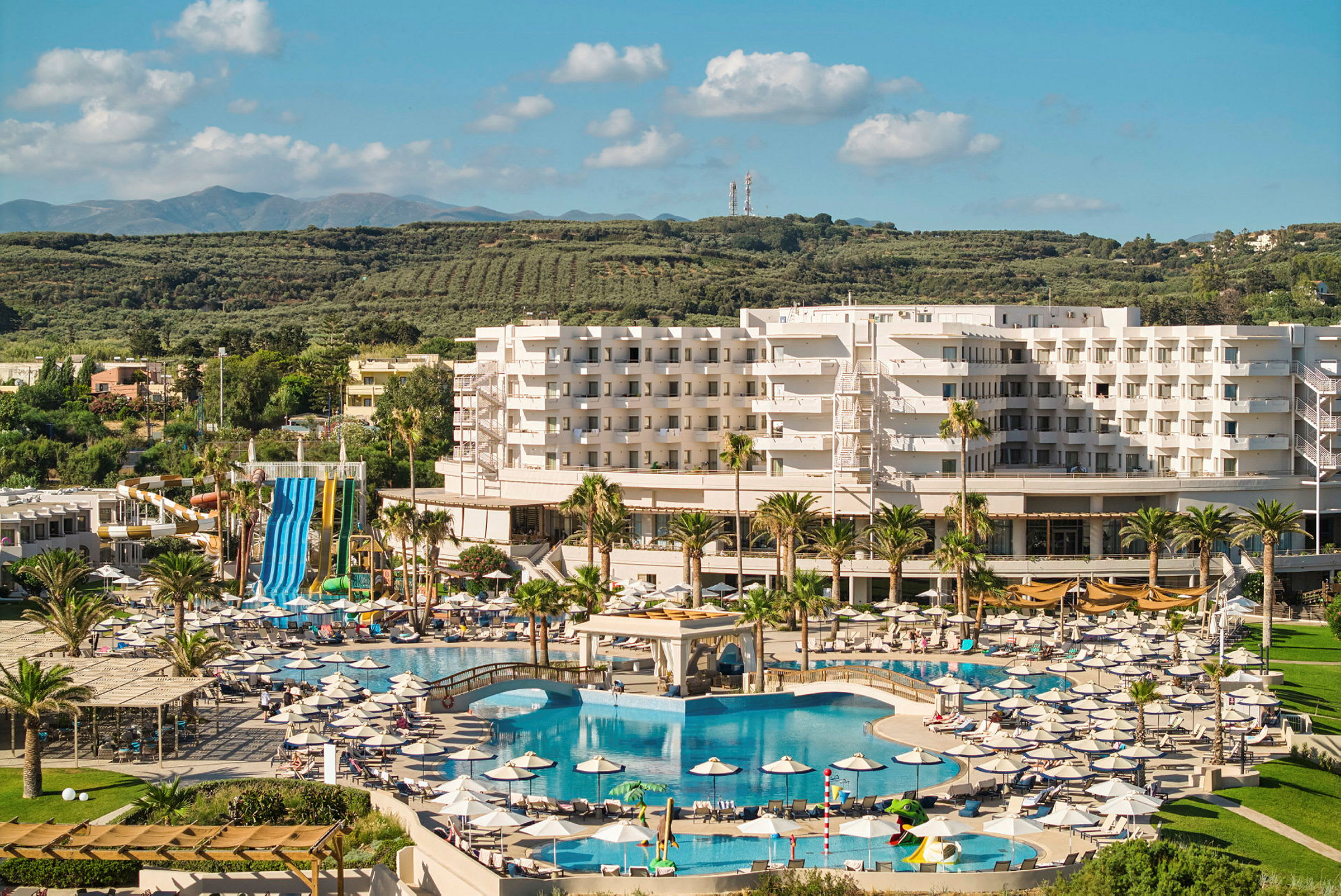Resort med ett stort poolområde och vattenrutschbanor, omgiven av grönska. (AI-genererad text)