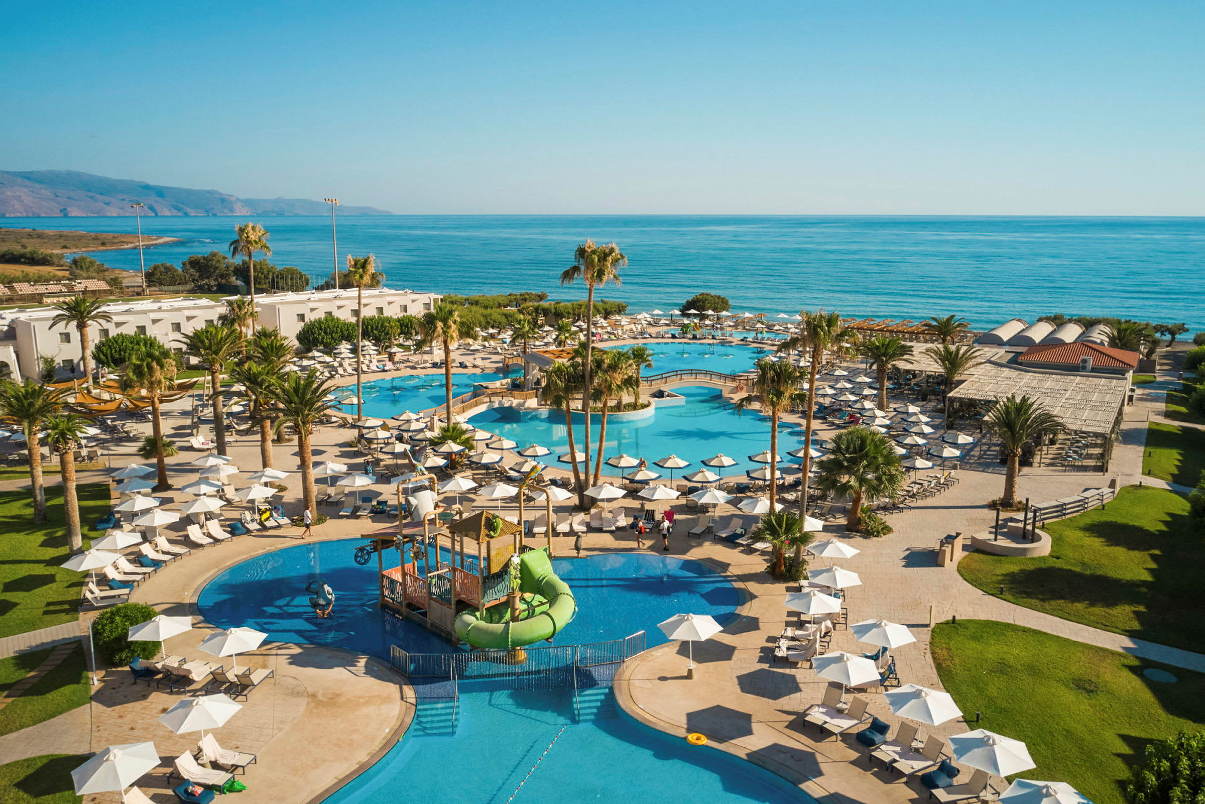 En vy över en resort med pooler och parasoller nära havet. (AI-genererad text)