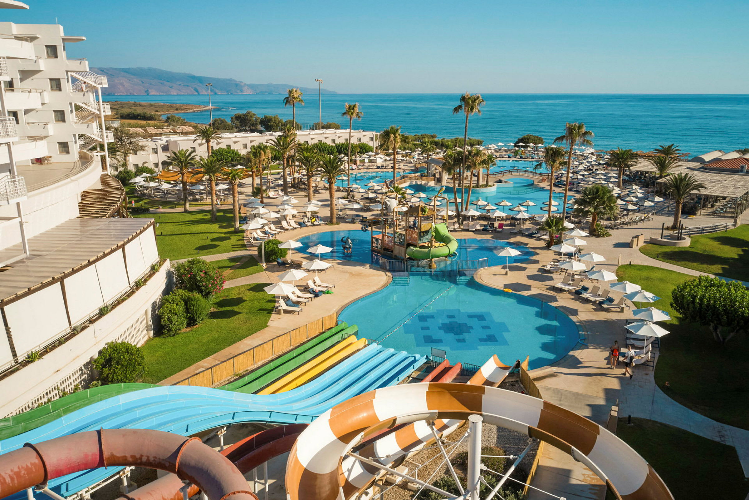 Vy över hotellpooler och vattenrutschbanor nära havet. (AI-genererad text)