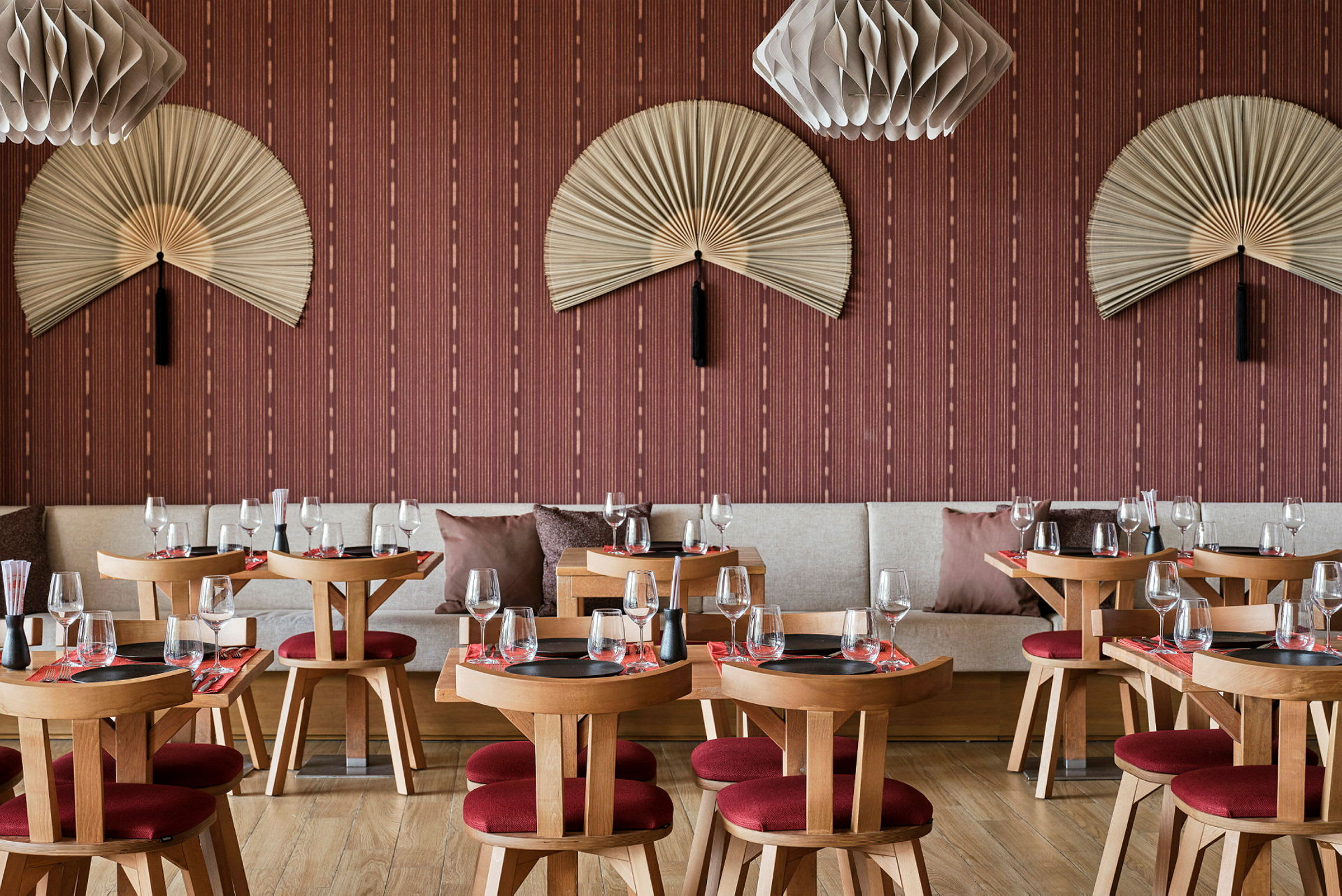 En restaurang med träbord och röda stolar, dekorerade med vägghängda solfjädrar och moderna lampor. (AI-genererad text)