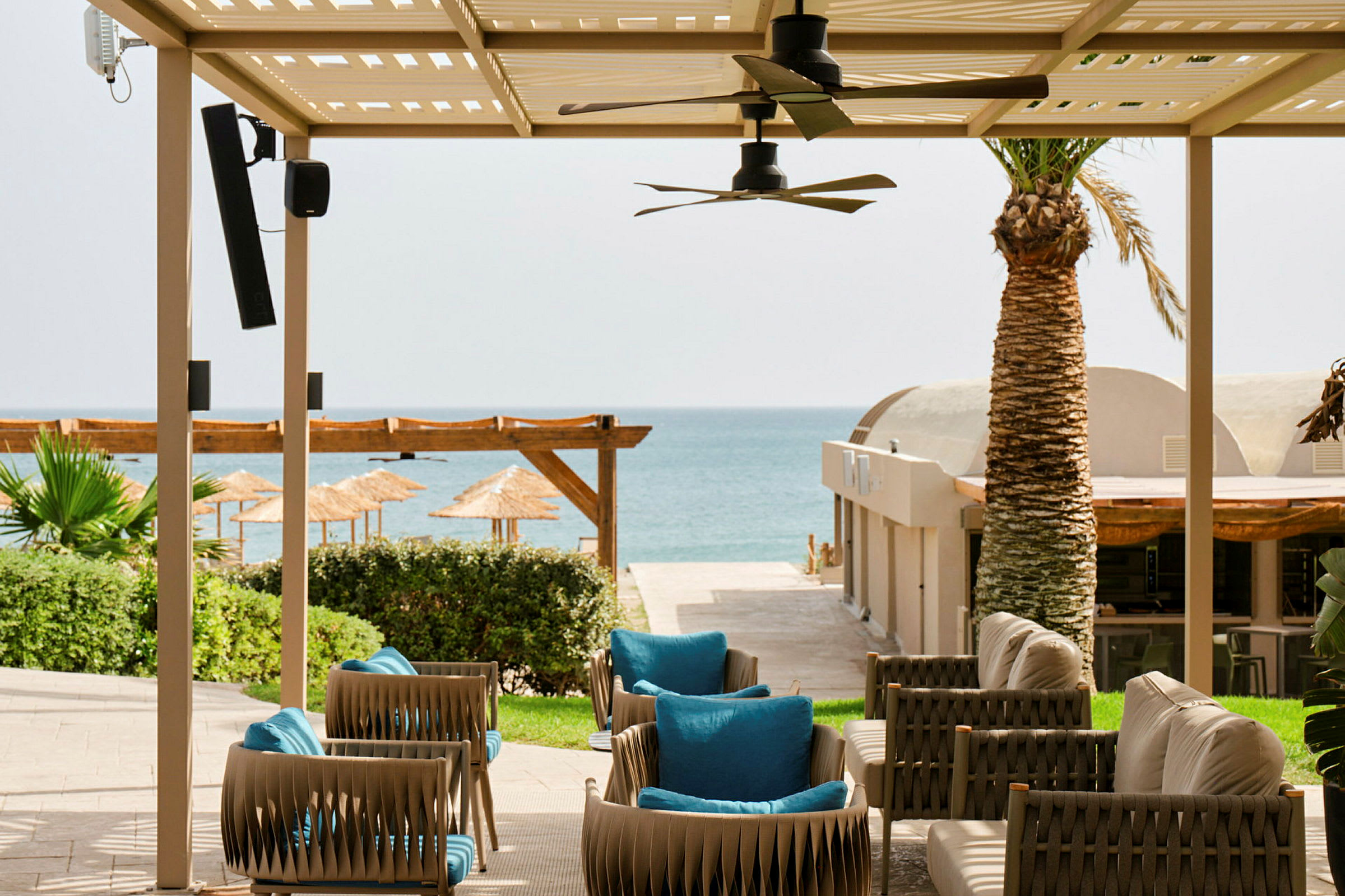 Trädgårdsmöbler under en pergola med utsikt mot en sandstrand och havet i bakgrunden. (AI-genererad text)