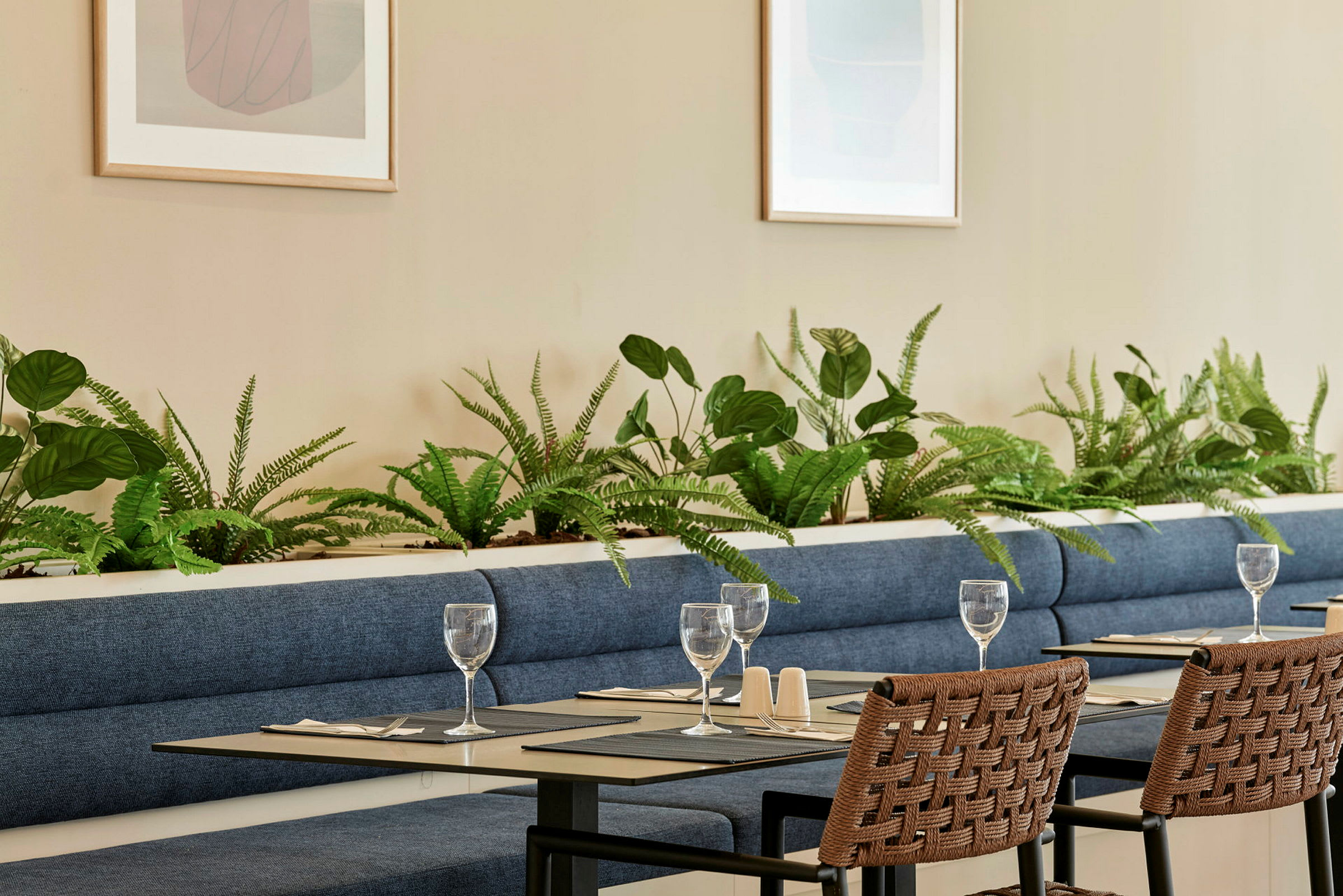 Ett restaurangområde med blå soffor, dekorerade med gröna växter och dukade bord. (AI-genererad text)