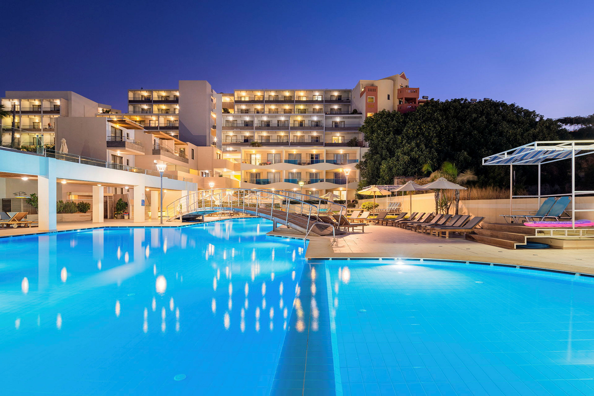 Hotellområde med en belyst pool och solstolar under kvällen. (AI-genererad text)