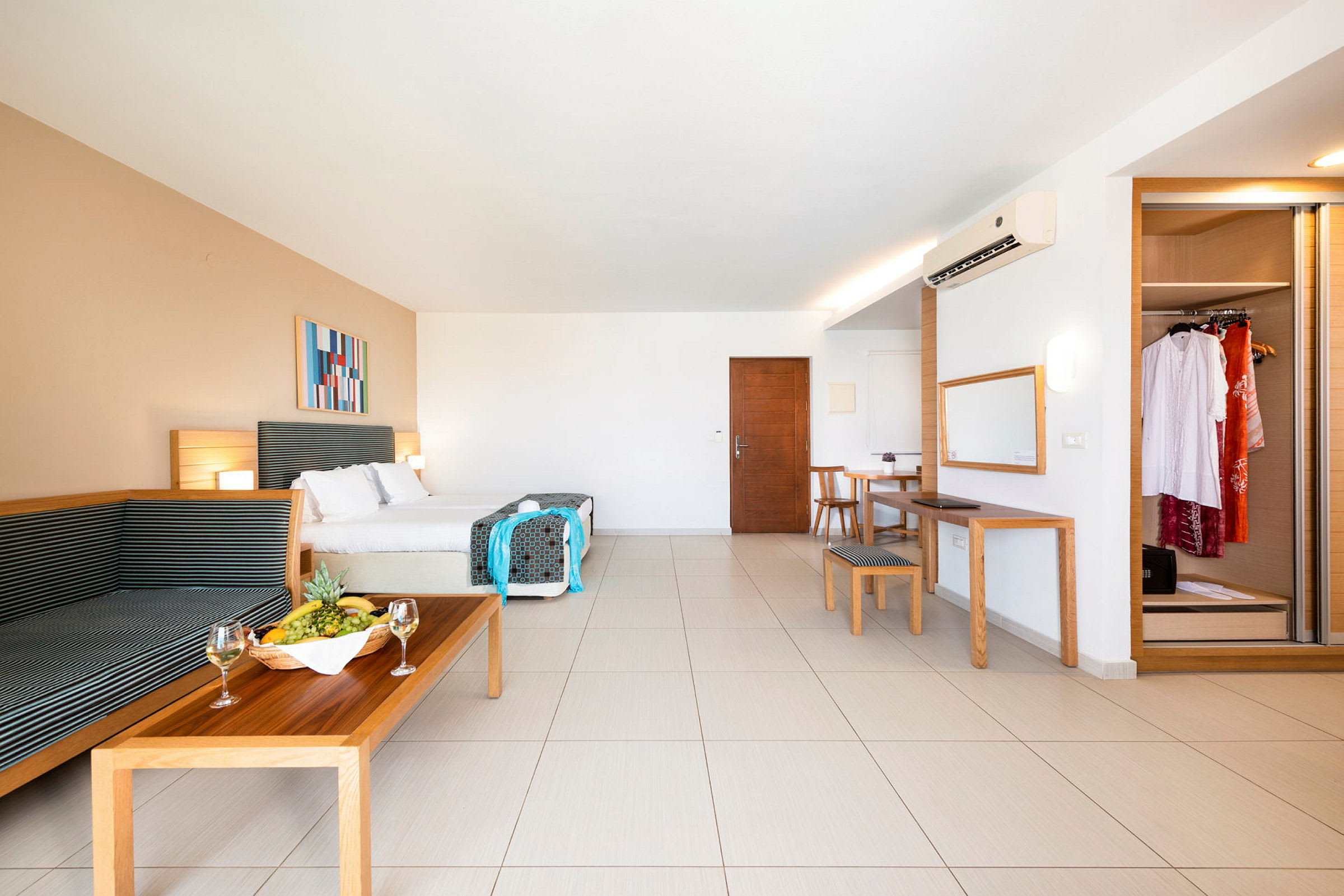 Ett rymligt hotellrum med dubbelsäng, sittgrupp, matbord, spegel och garderob. En fruktskål och vinglas står på soffbordet. (AI-genererad text)