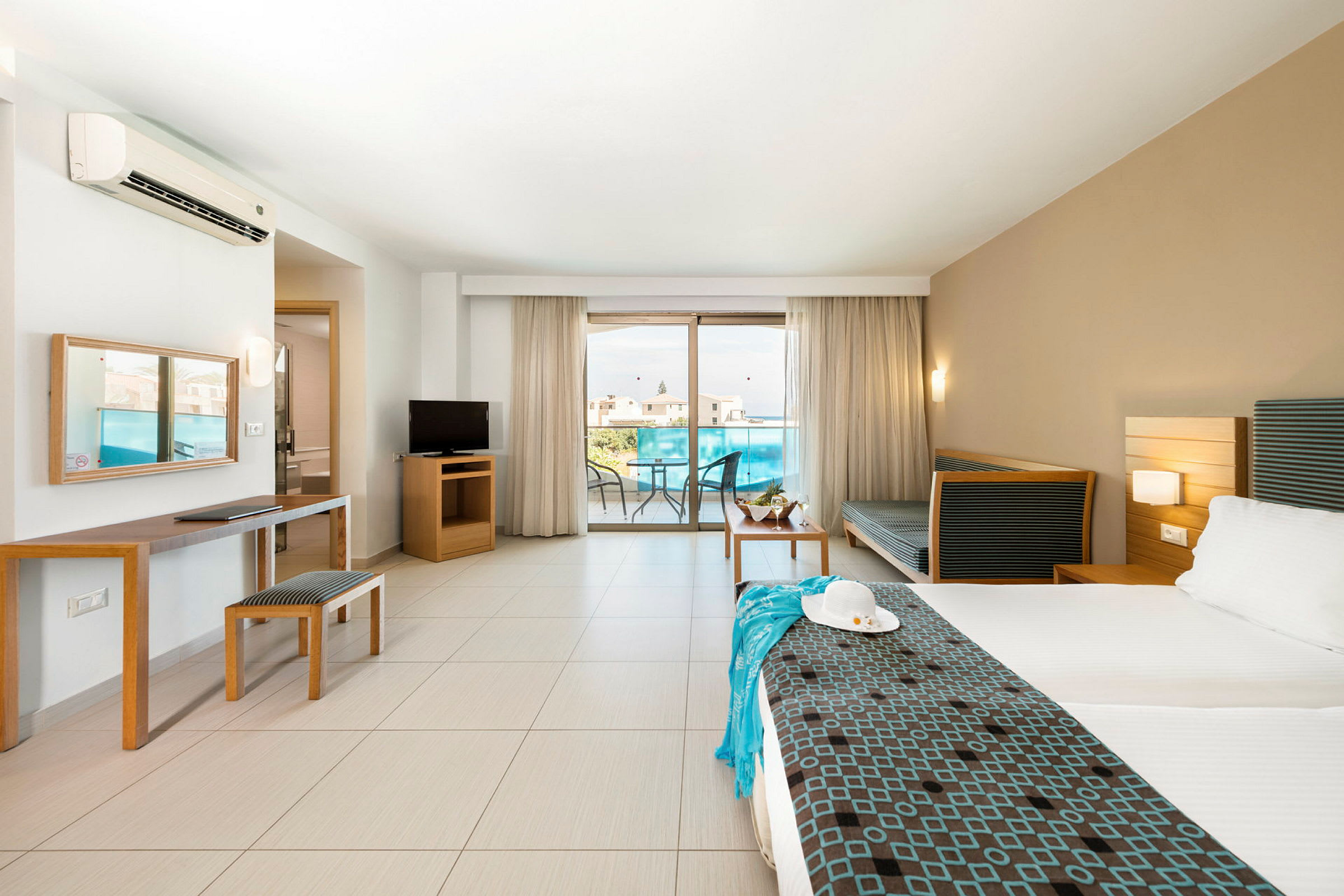 Ett hotellrum med en dubbelsäng, sittmöbler, TV och en balkong med utsikt. (AI-genererad text)