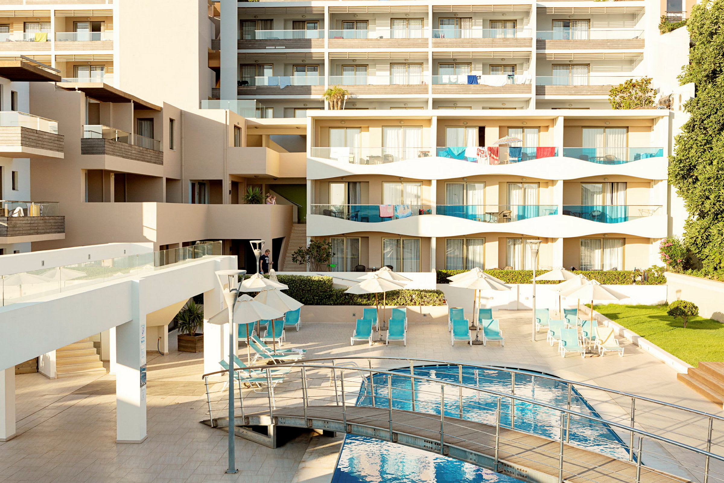 En modern hotellbyggnad med balkonger, solstolar vid en pool och grönska. (AI-genererad text)