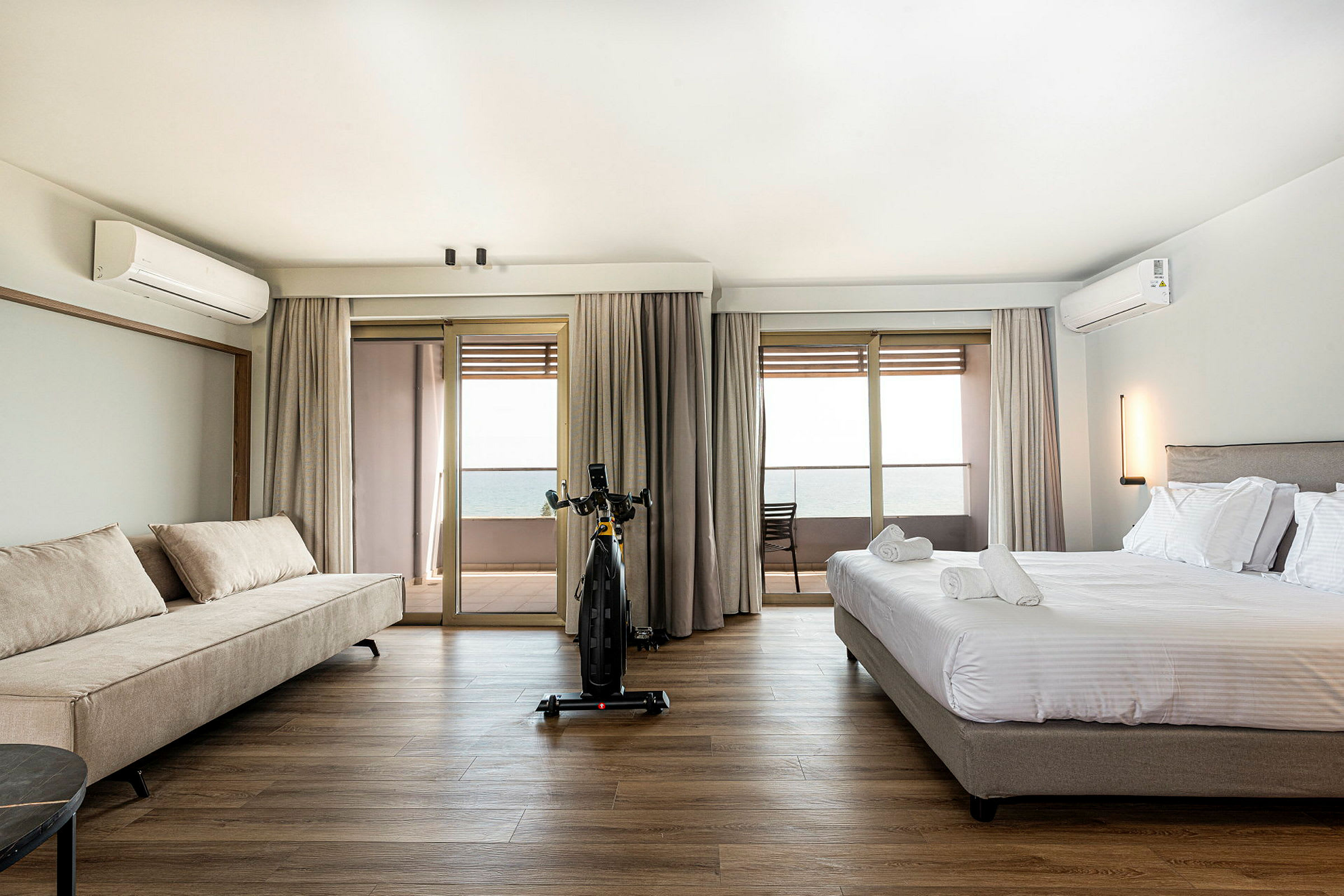 Ett hotellrum med en säng och en soffa, utsikt mot en balkong och havet. (AI-genererad text)