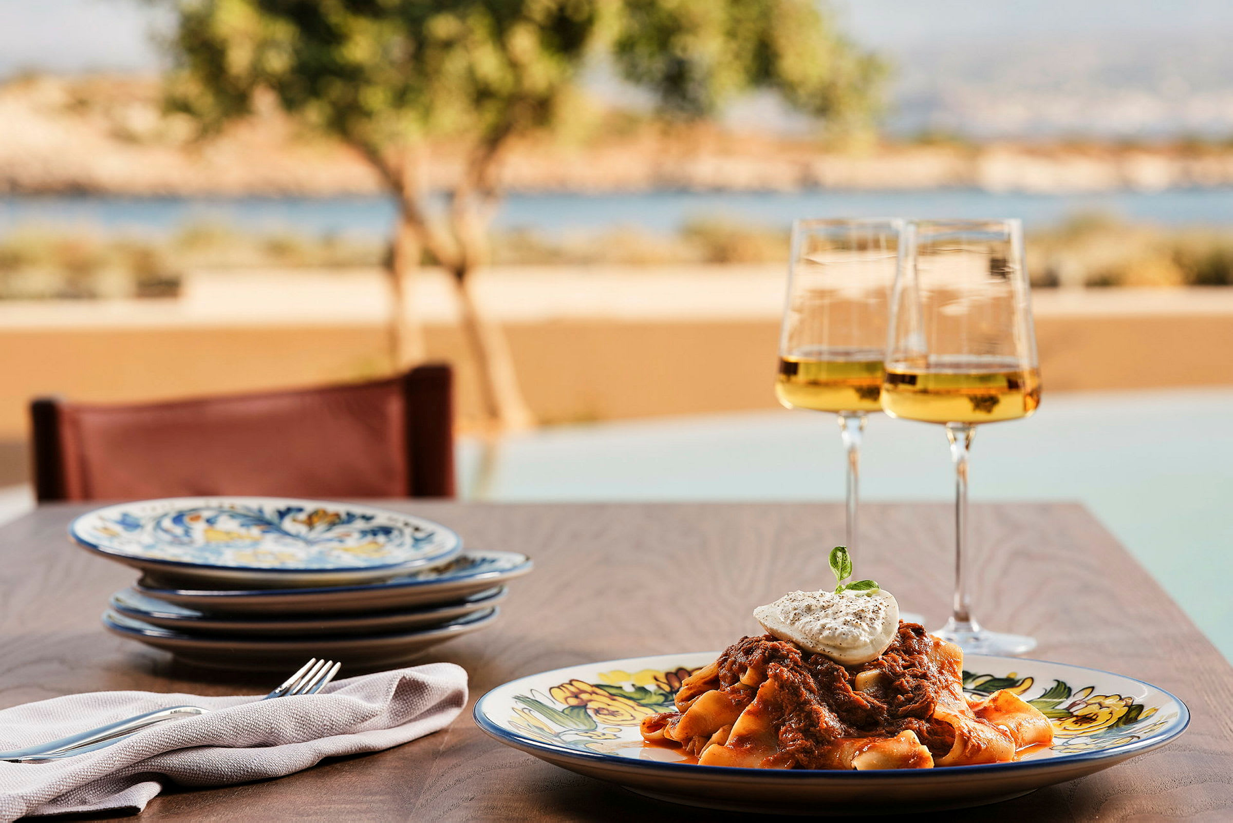 Tallrik med pasta och ett glas vitt vin på ett bord med utsikt mot natur. (AI-genererad text)