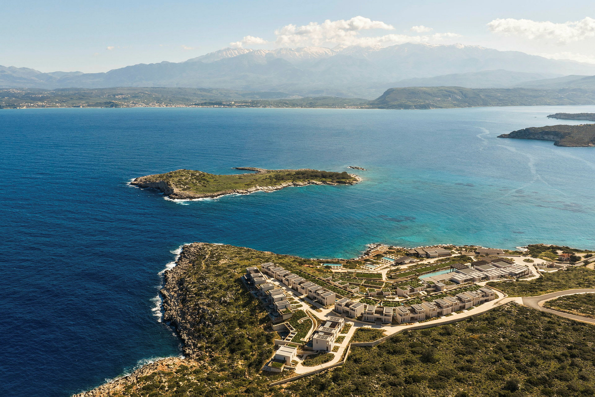 Flygfoto av en kust med klarblått vatten och små öar. En resort med byggnader och pool syns längs kusten. (AI-genererad text)