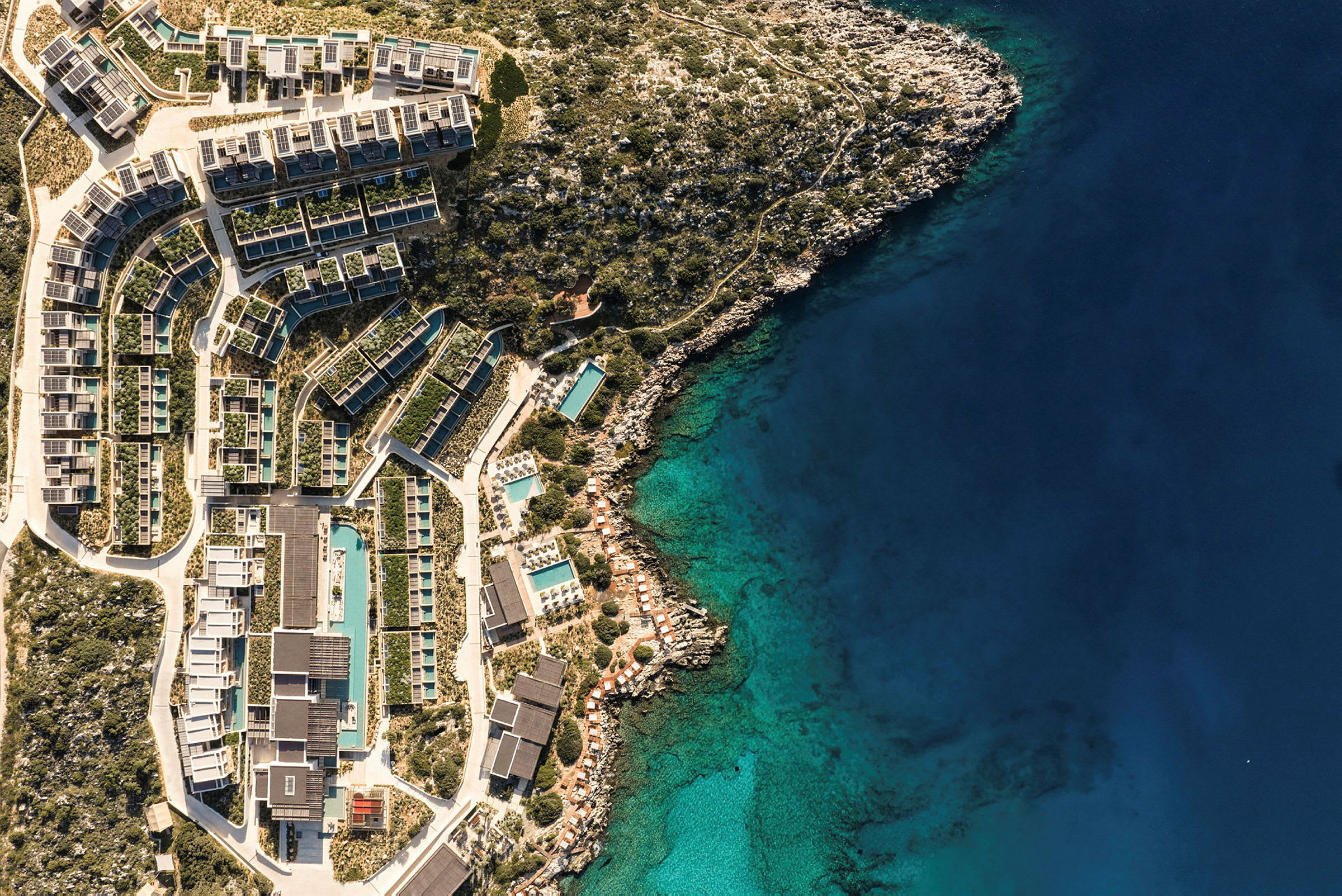 Flygfoto av en resort med byggnader och pooler omgivna av grönska vid kustlinjen. (AI-genererad text)