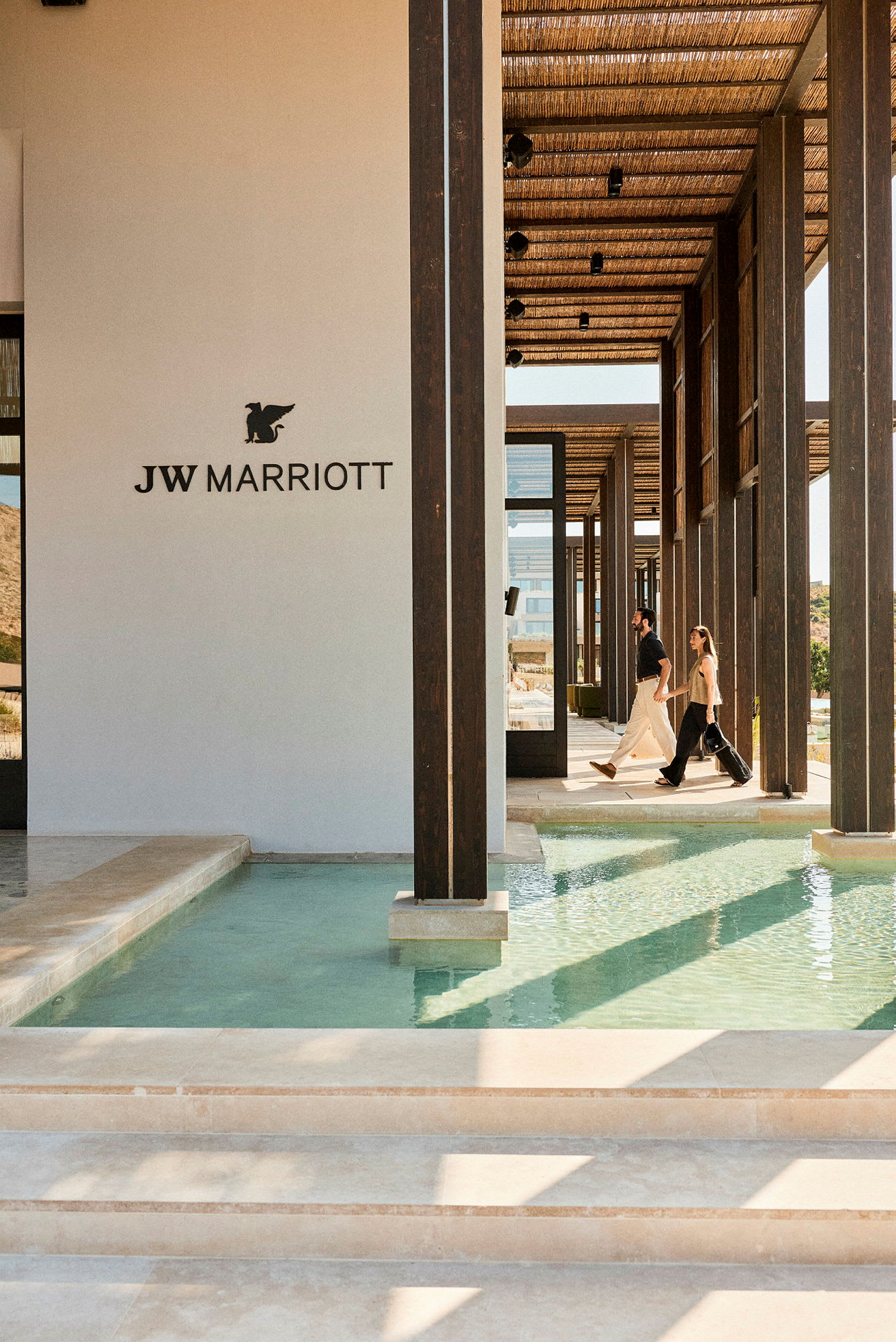 Bild på en modern byggnad med JW Marriott-logotypen, där människor går längs en gång med vatten på båda sidor. (AI-genererad text)