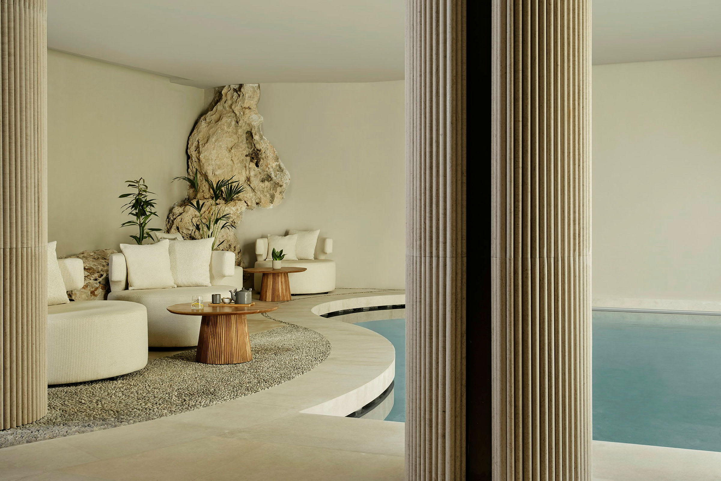Ett elegant inomhusområde med sittmöbler, träbord och en pool, omgiven av sten- och växtdekorationer. (AI-genererad text)