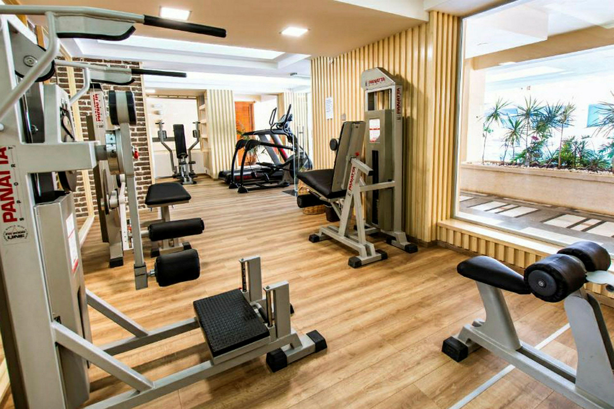 Ett gym med olika träningsmaskiner och vikter, bredvid en fönstervägg. (AI-genererad text)