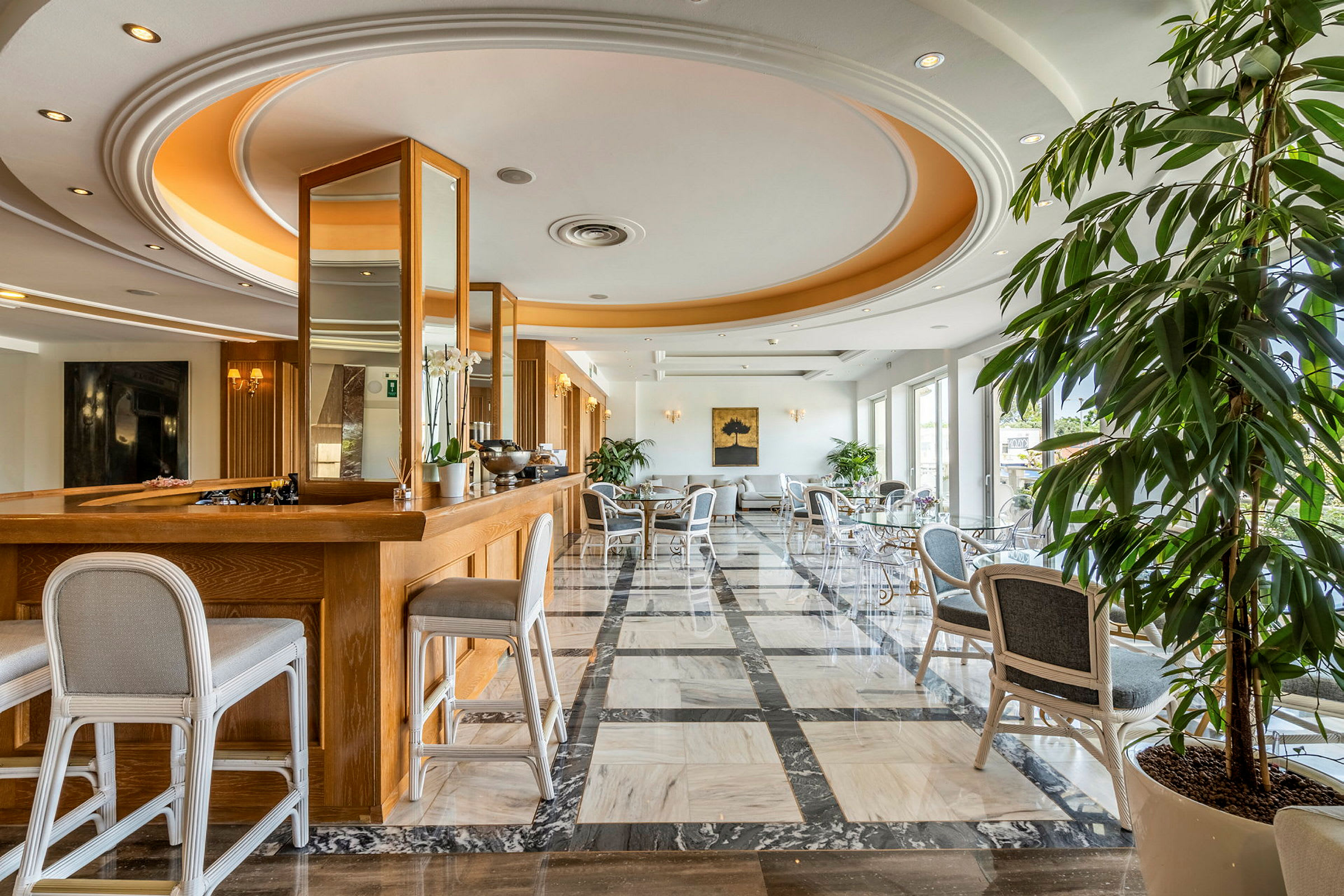 Ett elegant hotellrum med trämöbler och marmorgolv, stora fönster, samt växter och sittmöbler. (AI-genererad text)