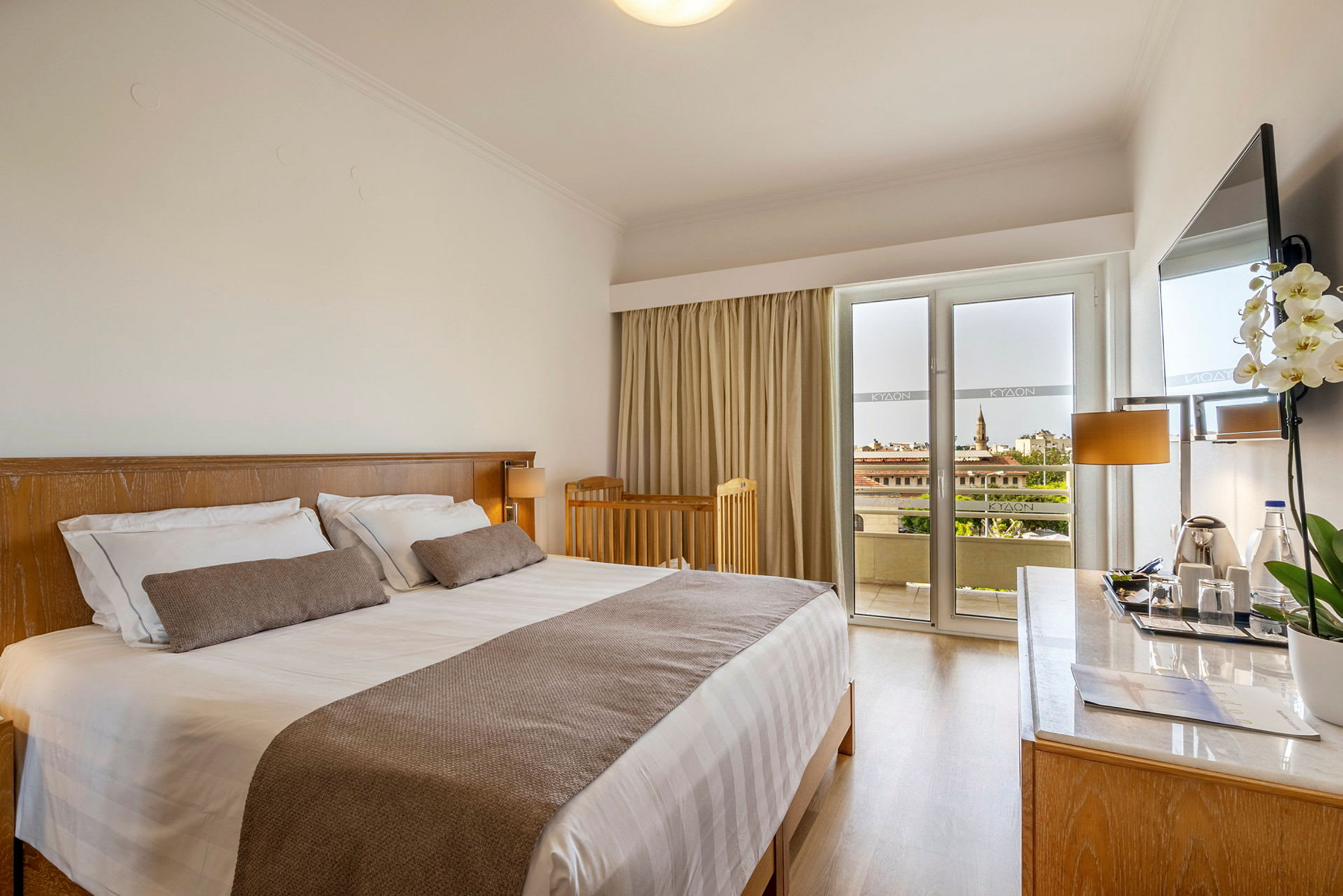 Ett hotellrum med en dubbelsäng, en barnspjälsäng, ett skrivbord med en spegel och en balkong med utsikt. (AI-genererad text)