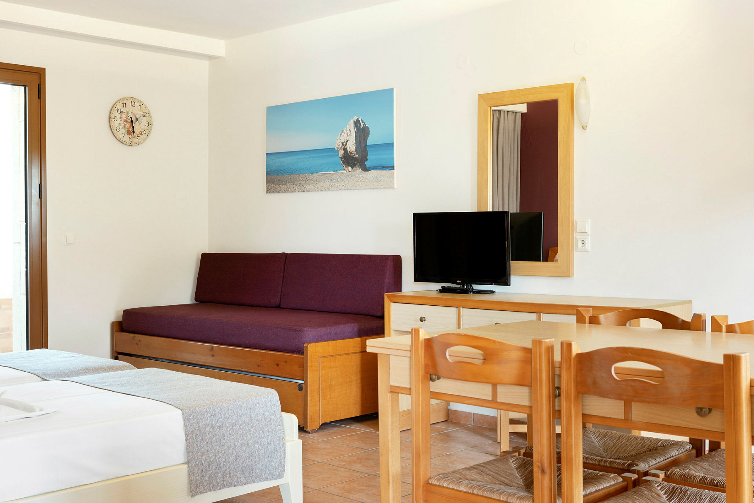 Inredning av ett hotellrum med en bäddsoffa, ett bord med stolar och en TV. (AI-genererad text)