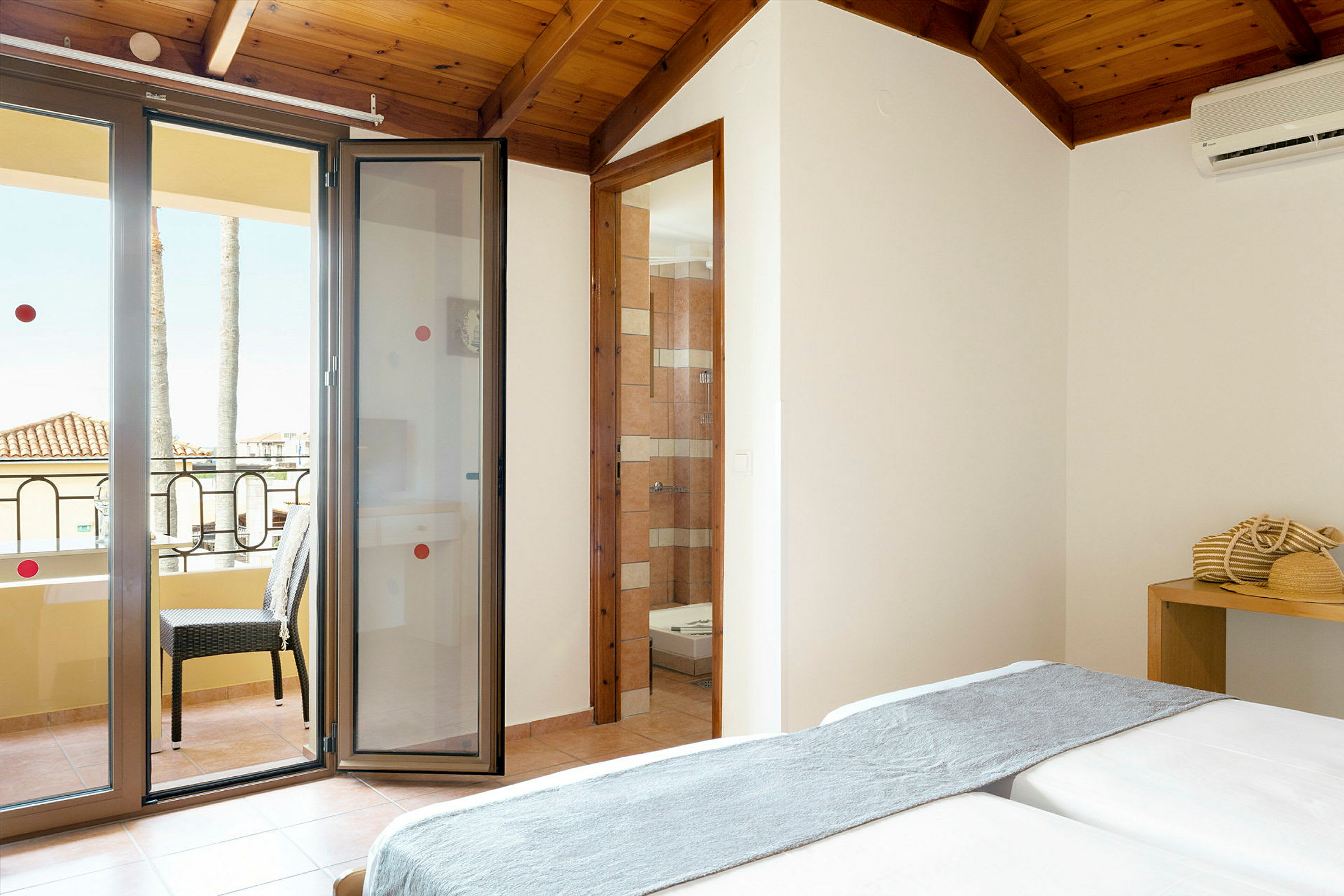 Ett hotellrum med en balkong och öppna dörrar, samt en sittplats och en mindre inredningsdetalj. (AI-genererad text)