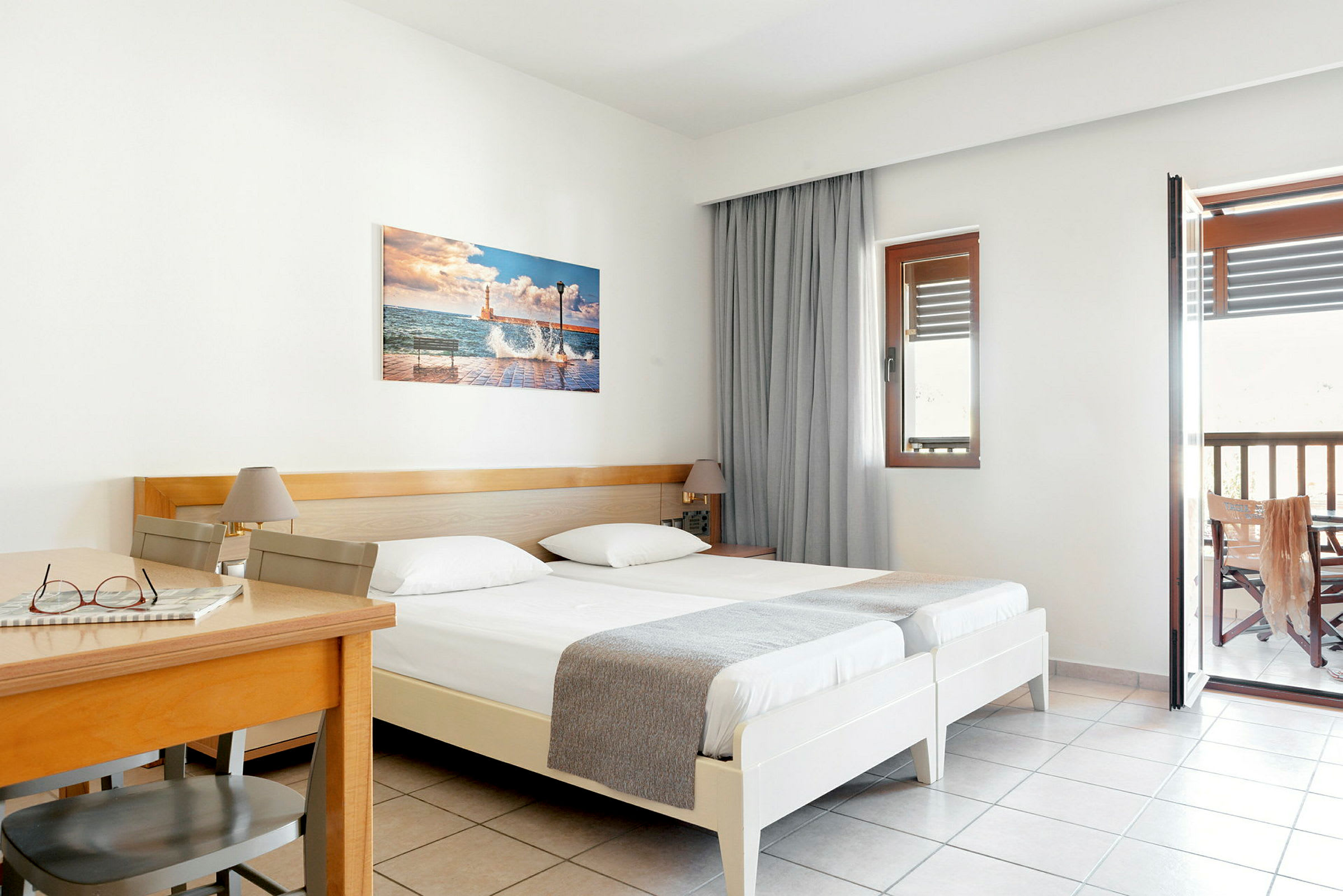 Hotellrum med två enkelsängar, ett träbord och stol samt balkong. (AI-genererad text)