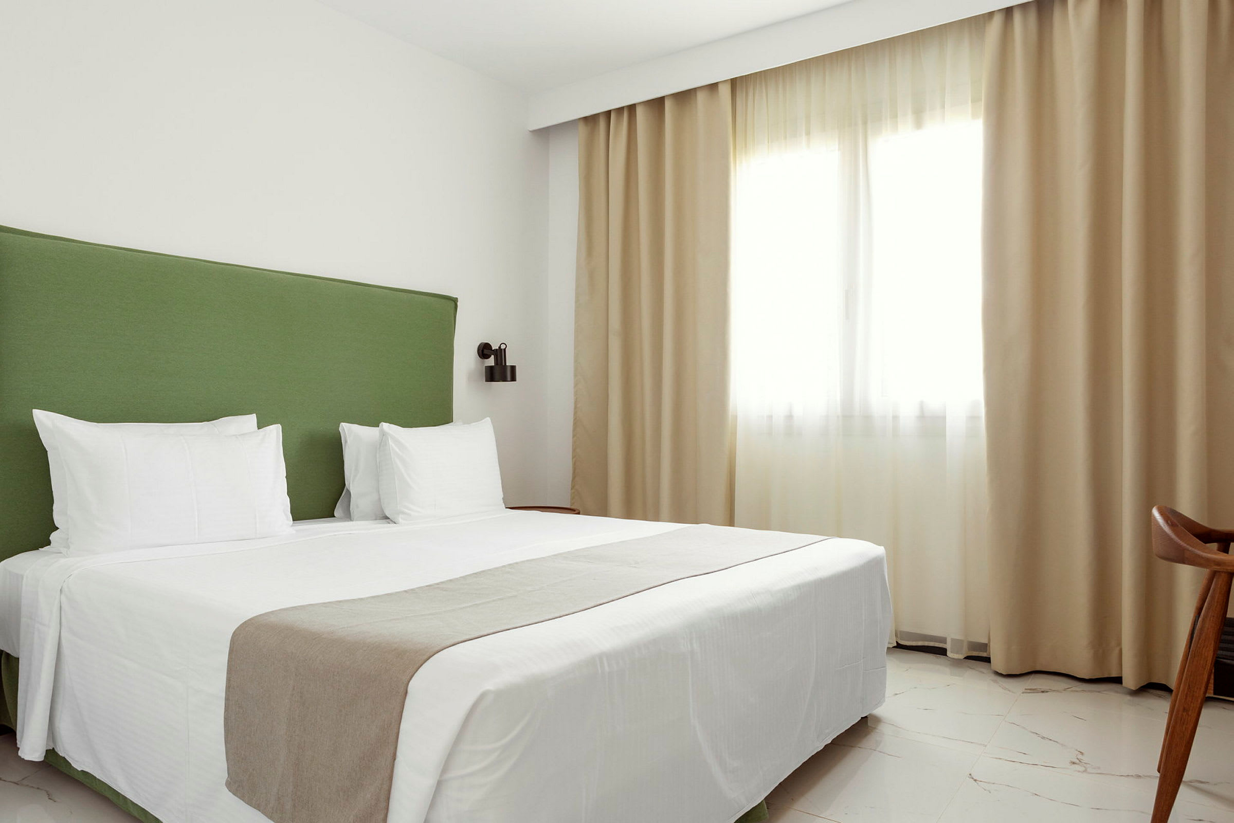 En hotelldubbelrum med en grön sänggavel och vita sängkläder. (AI-genererad text)