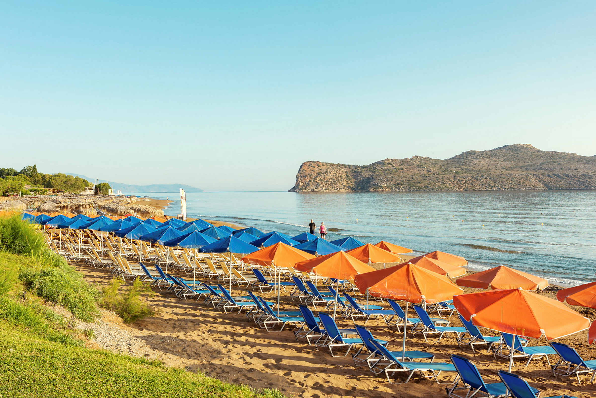 Strand med solstolar och parasoller, samt hav och klippor i bakgrunden. (AI-genererad text)