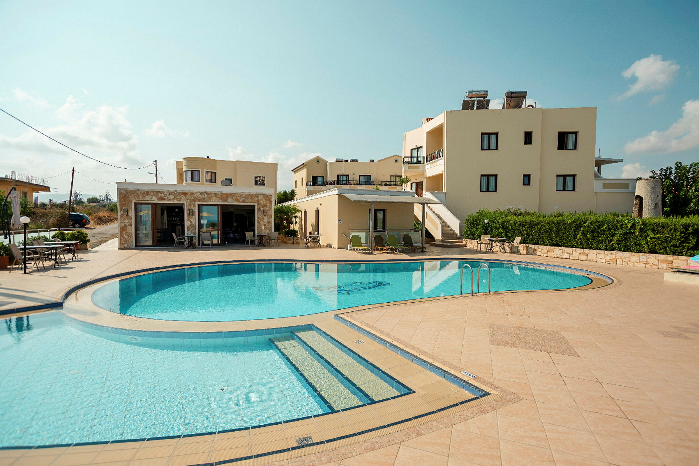 En pool med omgivande soldäck framför beige byggnader. (AI-genererad text)