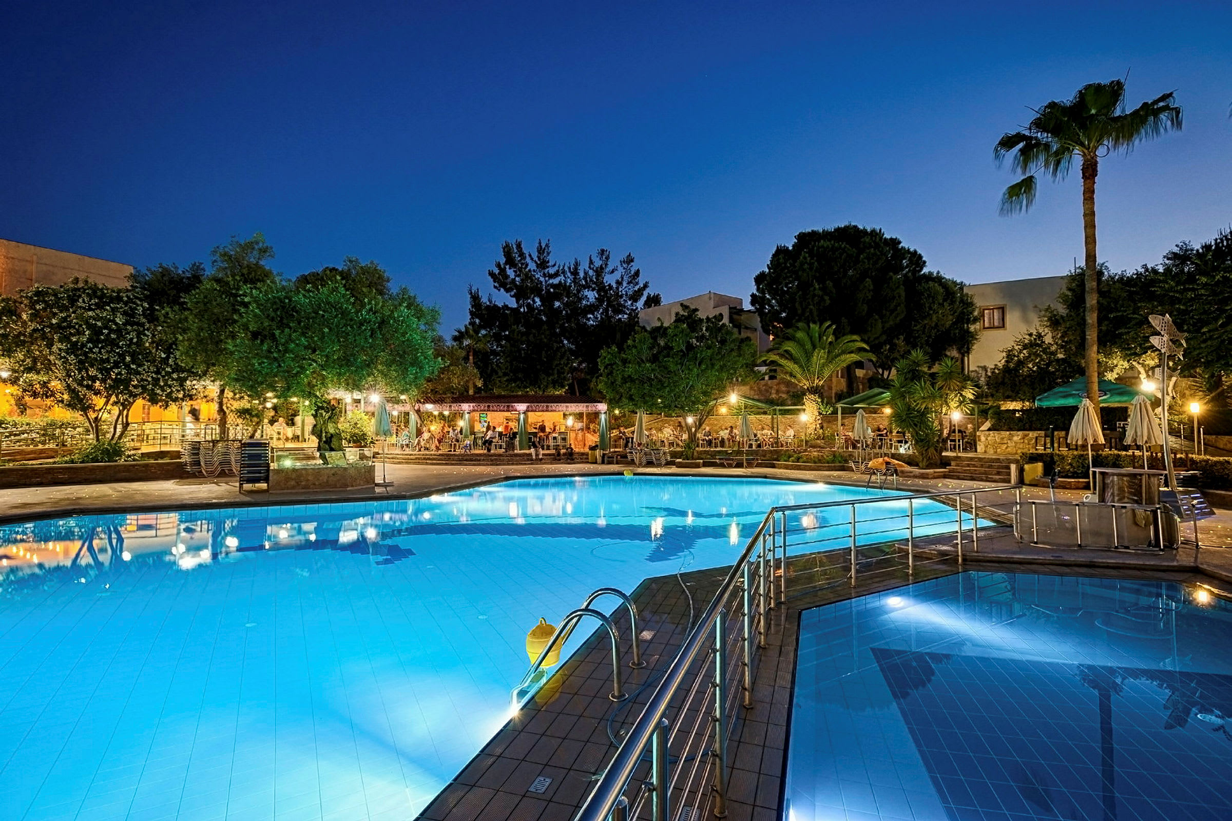 En upplyst swimmingpool med omgivande trädgårdsområde på kvällen. (AI-genererad text)