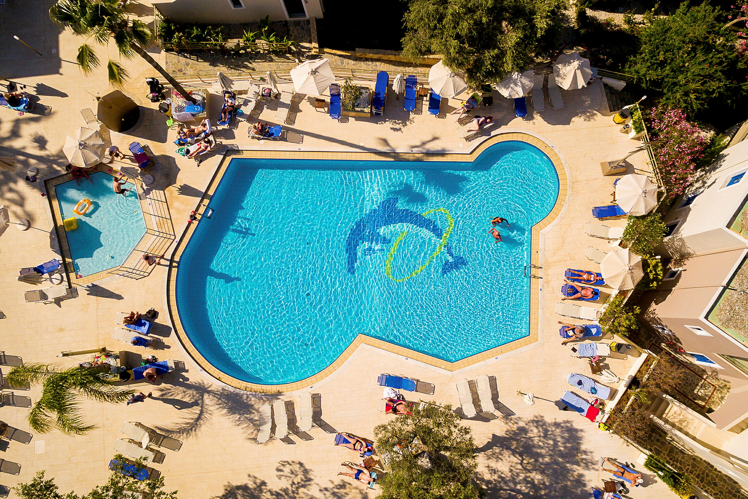 Utomhuspool med solsängar och parasoller samt några personer som badar. (AI-genererad text)