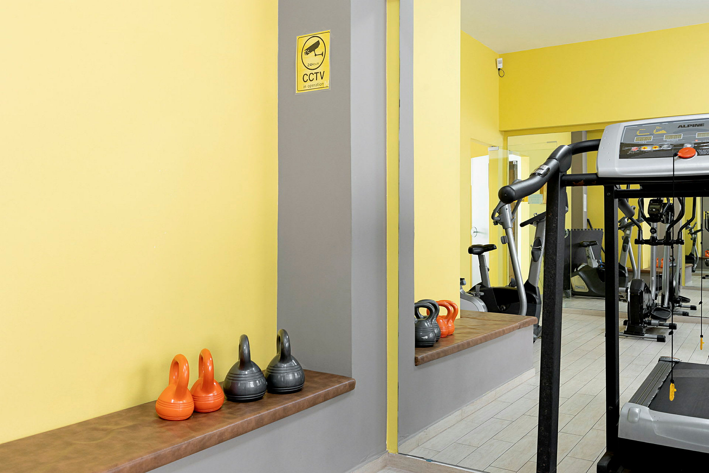 Ett gym med kettlebells och en löpmaskin. Väggar är målade gula. (AI-genererad text)