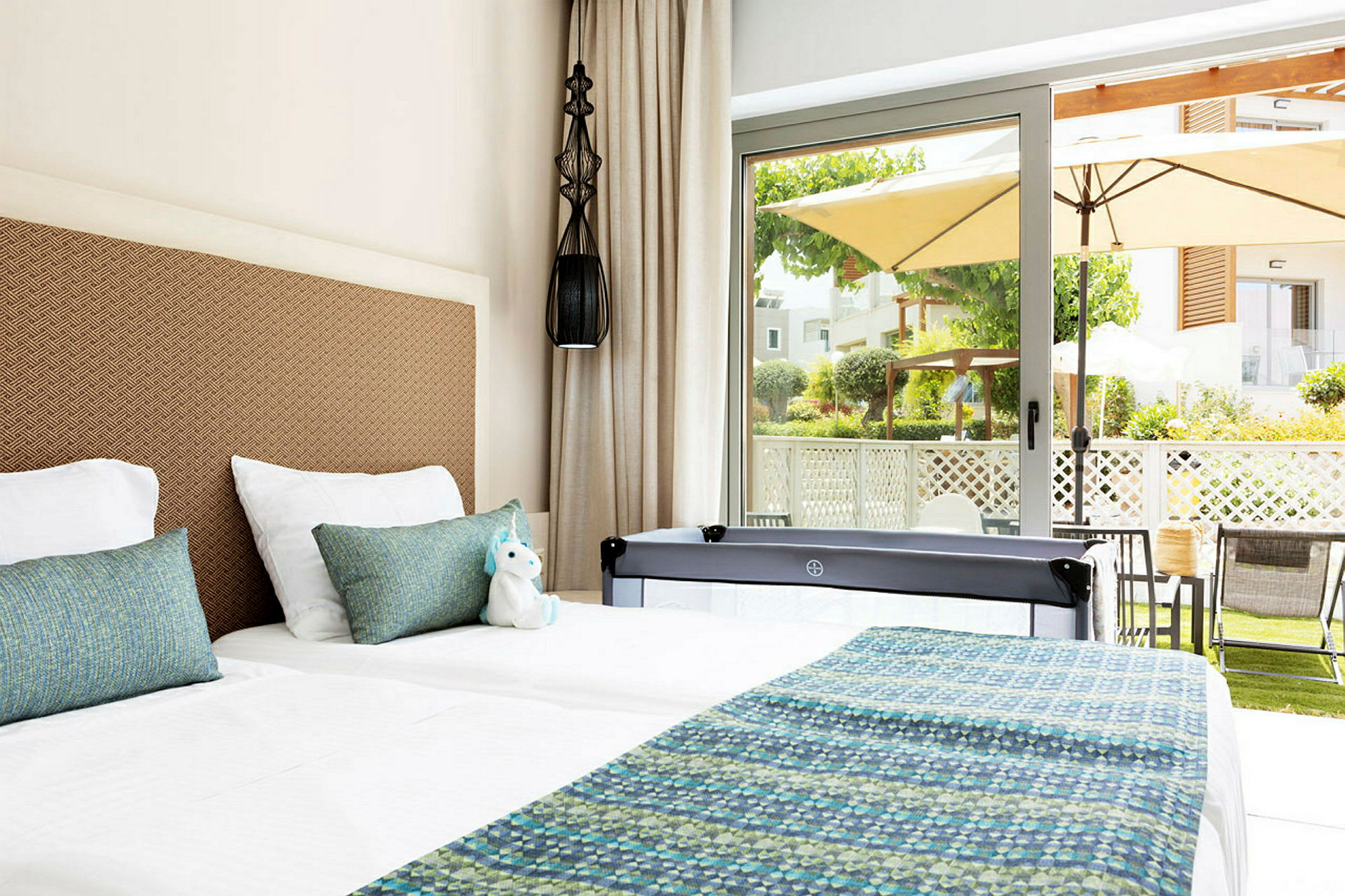 Hotellrum med två sängar, ljus inredning och utsikt över en terrass och trädgård genom stora glasdörrar. (AI-genererad text)