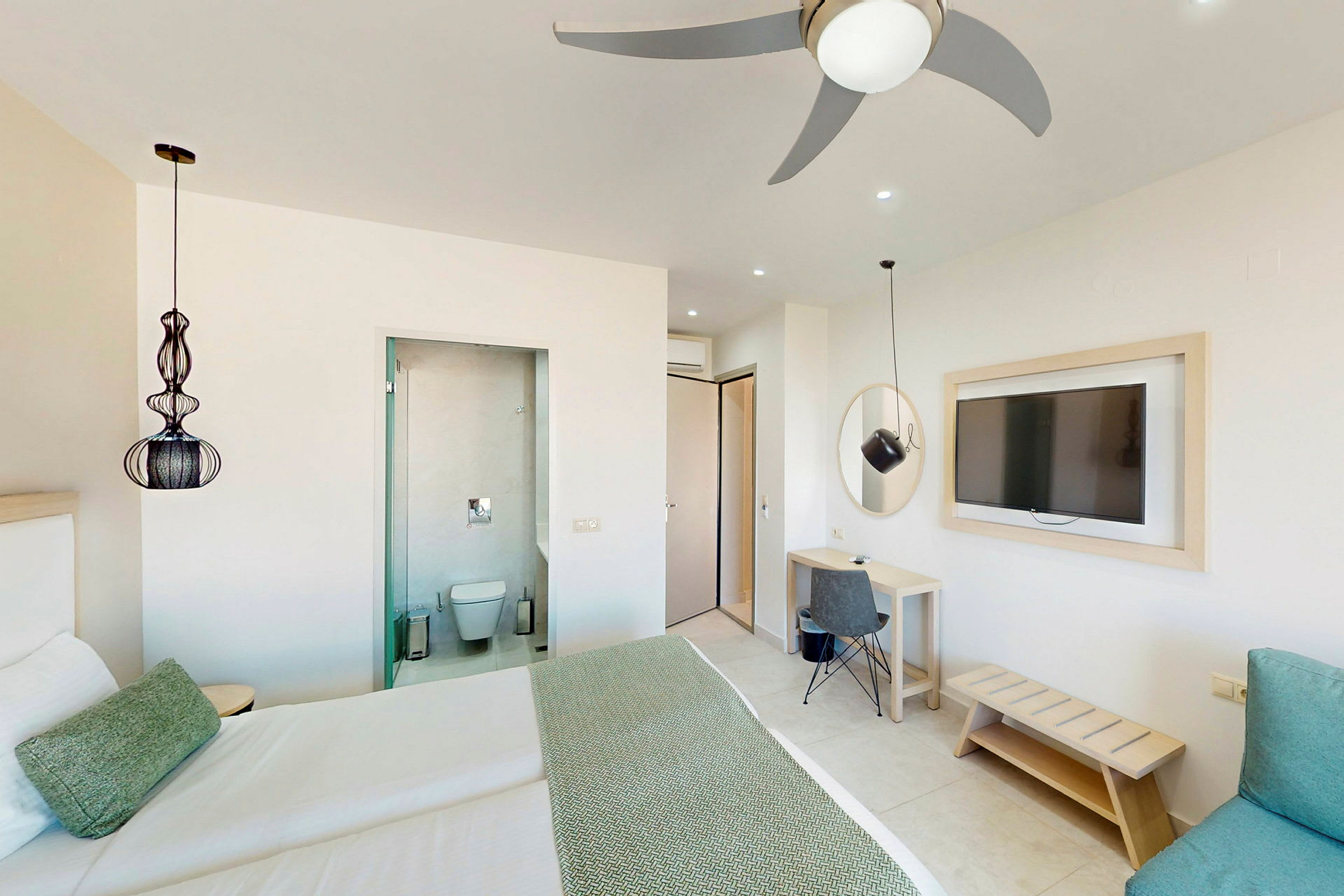 Hotellrum med en dubbelsäng, ett skrivbord, en väggmonterad TV och ingång till badrummet. (AI-genererad text)