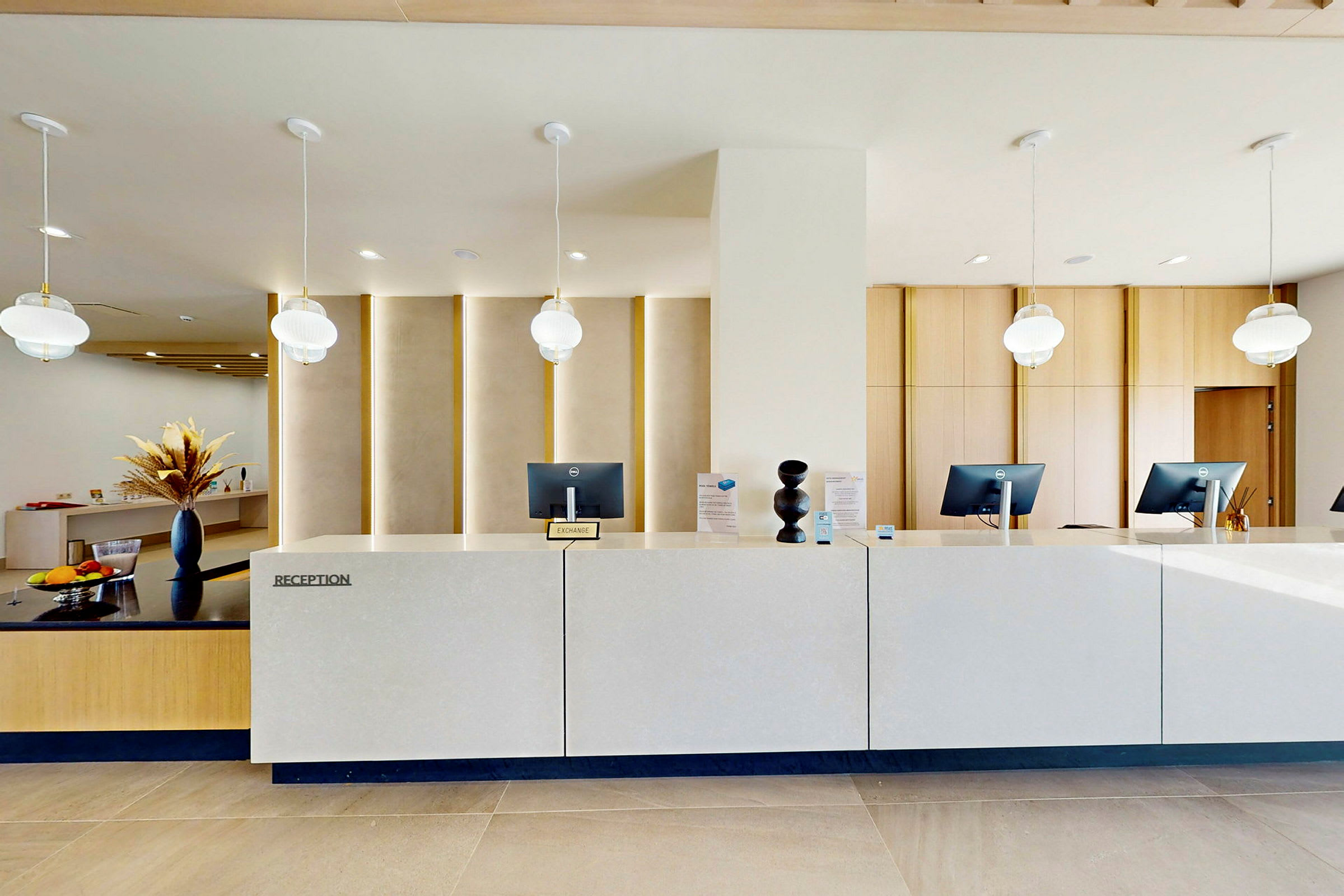 Hotellets reception med datorer på bänken och dekorativa lampor i taket. (AI-genererad text)