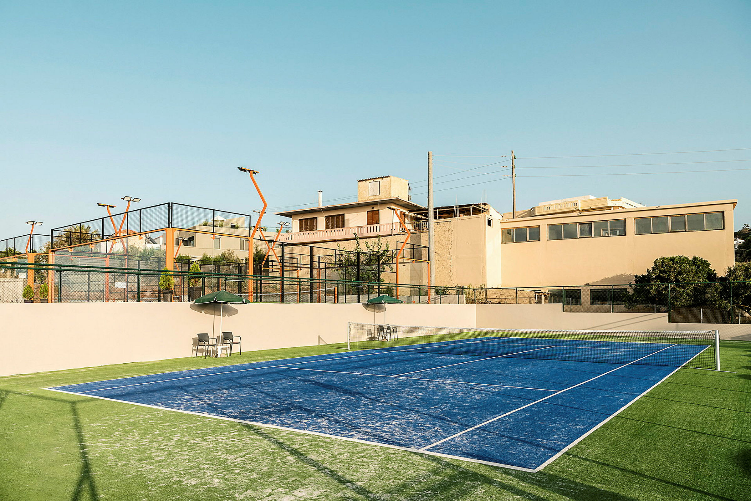 Blå padelplan med läktare i bakgrunden och omgivande byggnader. (AI-genererad text)