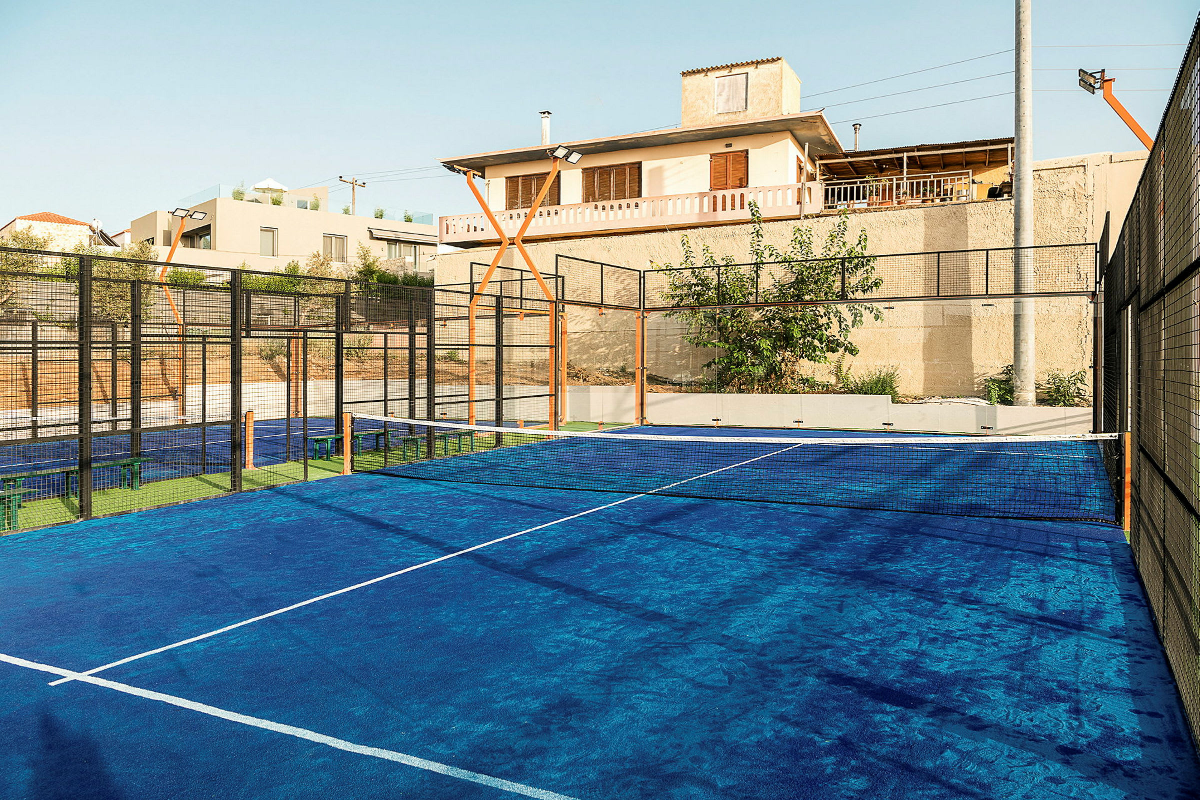 En blå padelbana med nätnät och omgivande byggnader. (AI-genererad text)