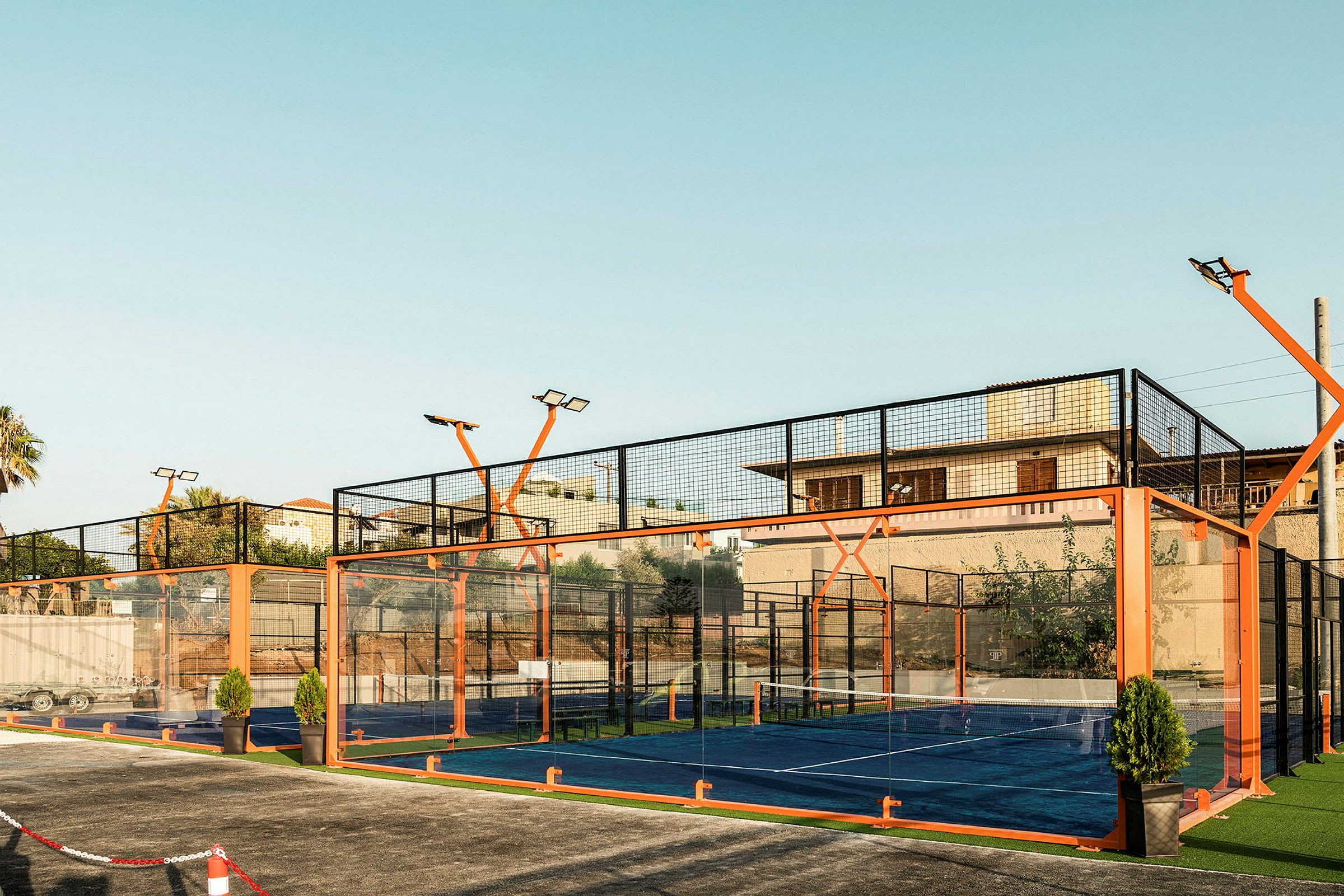 En utomhus padelbana omringad av glas och orange ställning. (AI-genererad text)