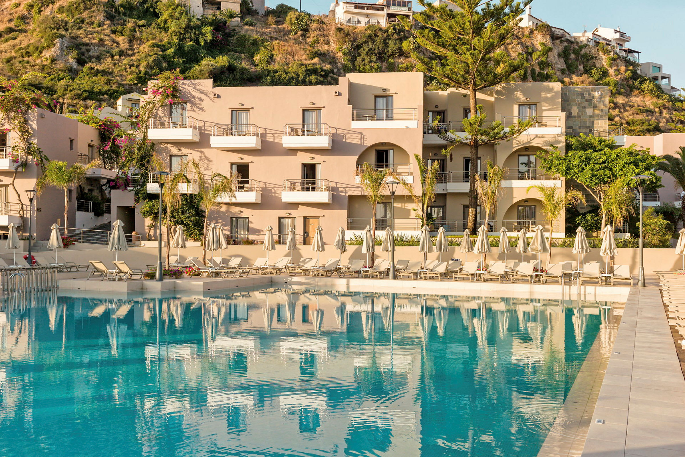 En hotellbyggnad med balkonger framför en pool med solstolar. (AI-genererad text)