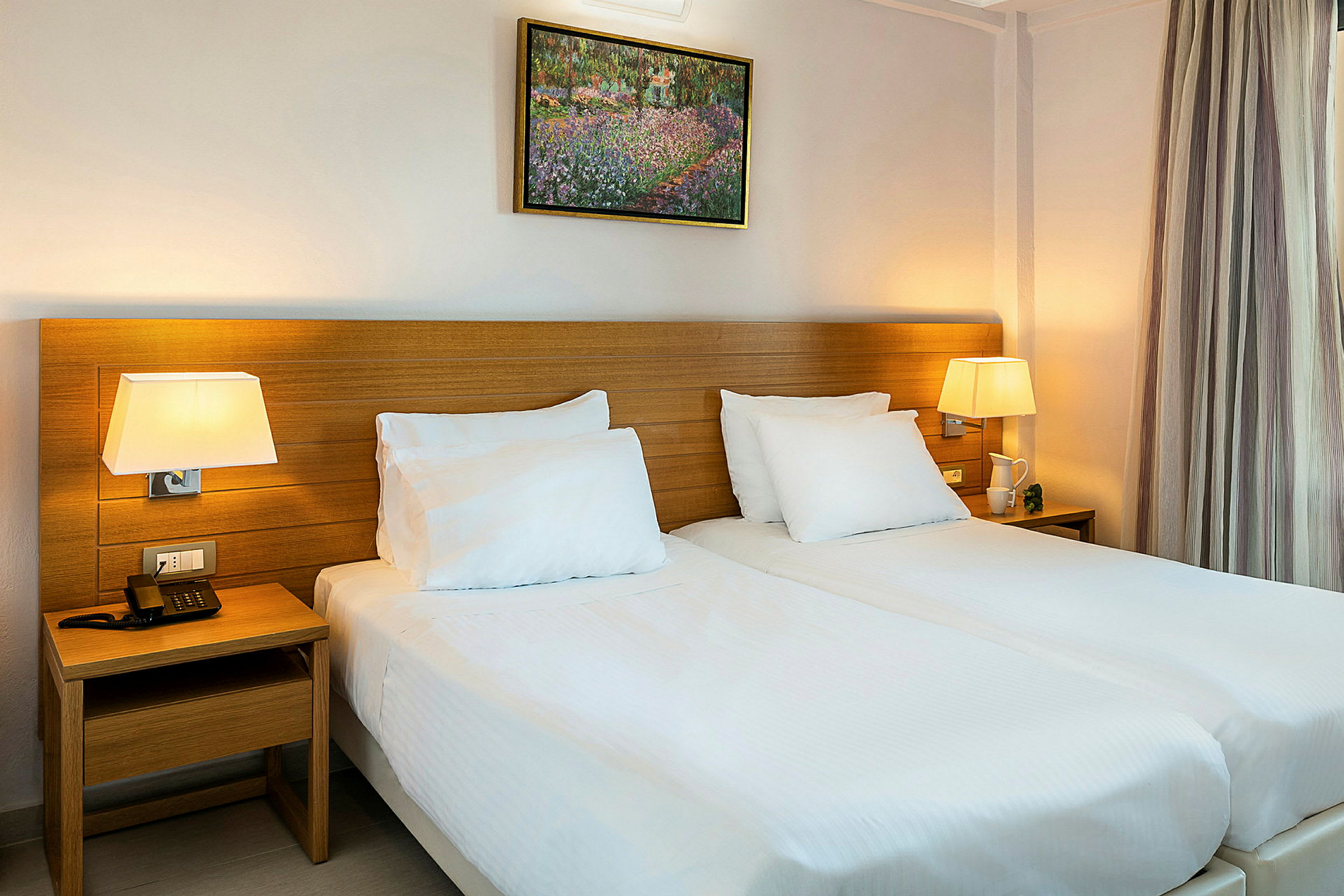 Ett hotellrum med två enkelsängar, sängbord med lampor och en tavla på väggen. (AI-genererad text)