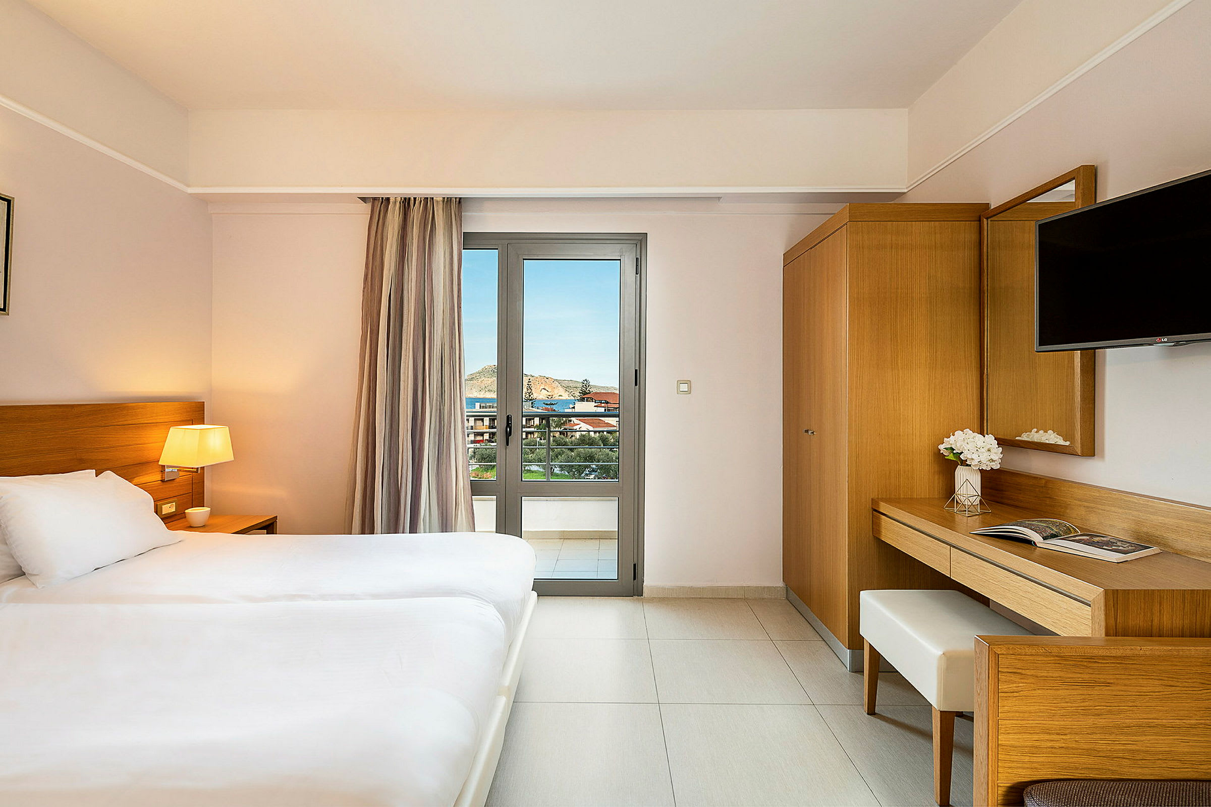 Ett hotellrum med en dubbelbädd, träinredning, skrivbord, TV, och en balkongdörr som erbjuder utsikt. (AI-genererad text)
