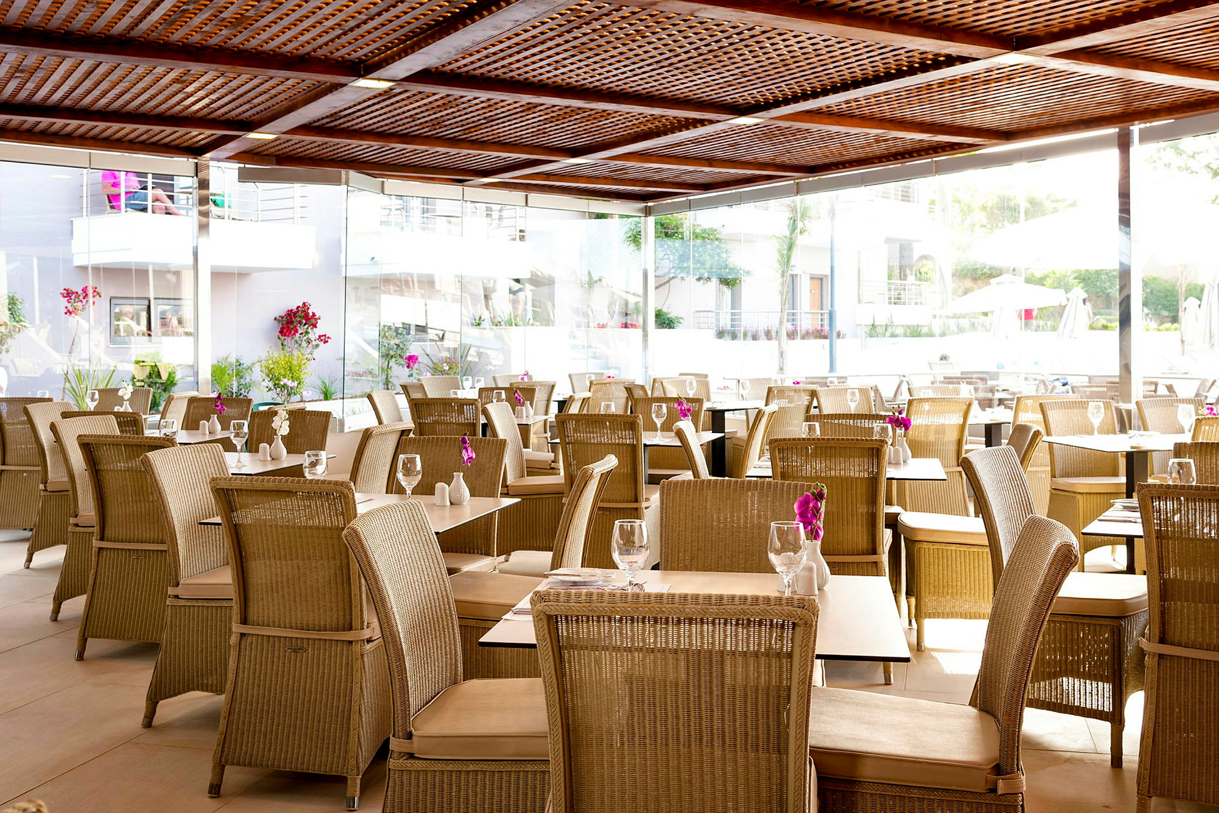 Restaurang med rottingmöbler och blommor på borden. (AI-genererad text)