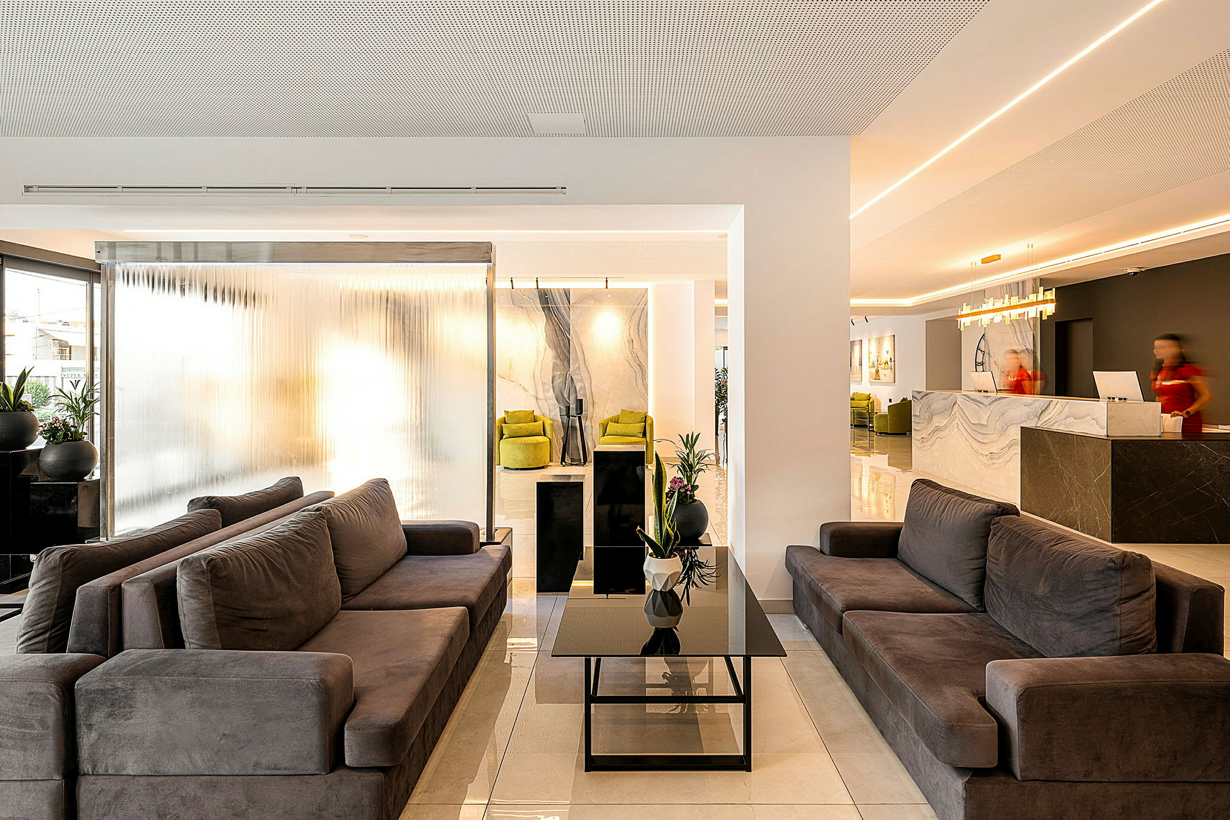 En modern hotellobby med bekväma soffor, ett glasbord och receptionen i bakgrunden. (AI-genererad text)