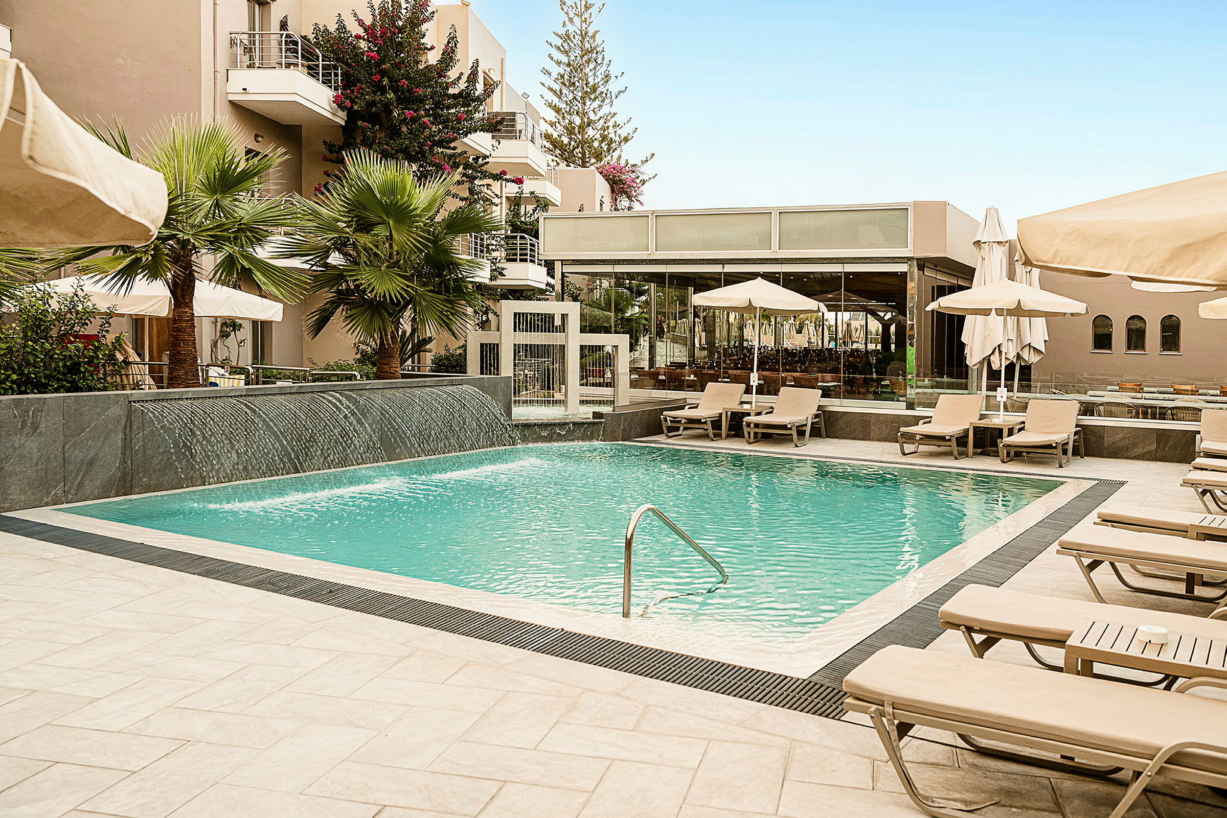 En pool omgiven av solstolar, parasoller och gröna växter vid ett hotellområde. (AI-genererad text)