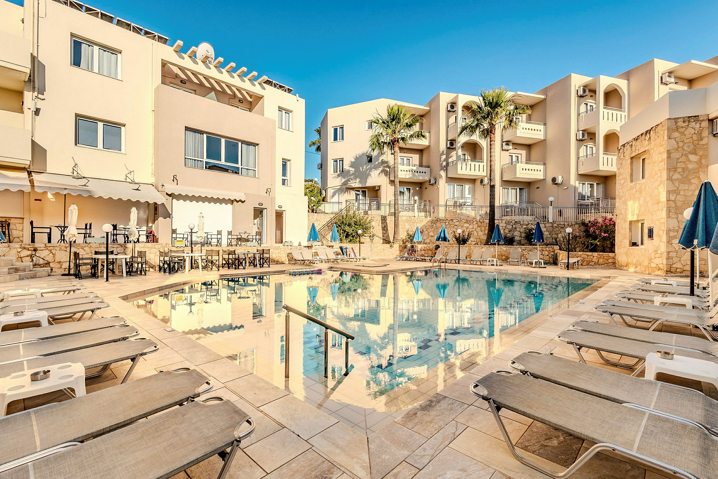 En hotellpool omgiven av solstolar och byggnader. (AI-genererad text)