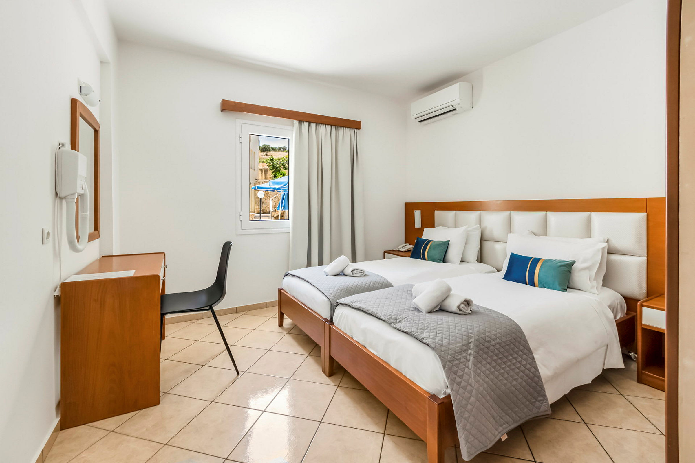 Ett hotellrum med två enkelsängar, skrivbord och stol, och ett fönster med utsikt. (AI-genererad text)